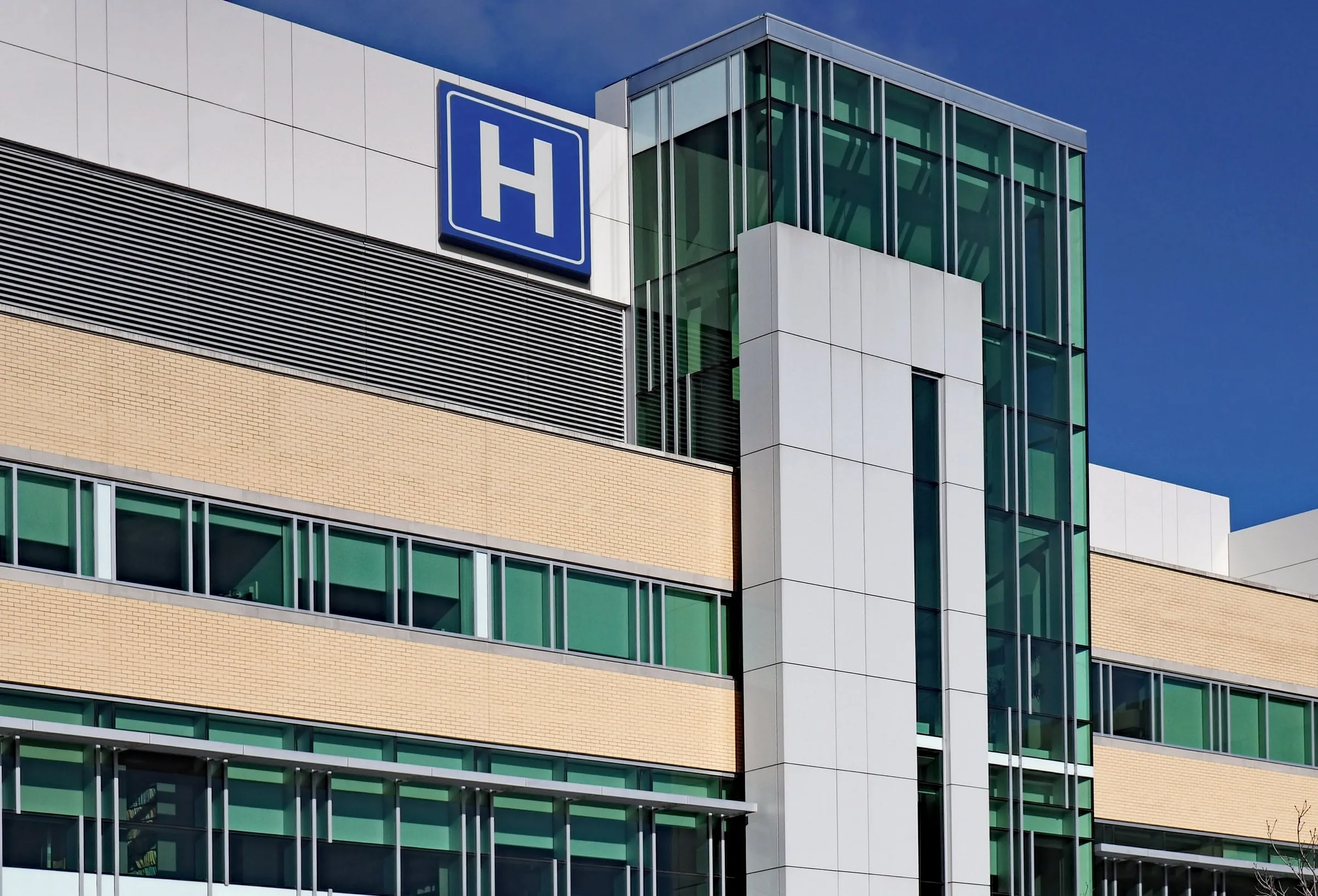 Modern hospital building with a large blue H sign above the entrance canopy