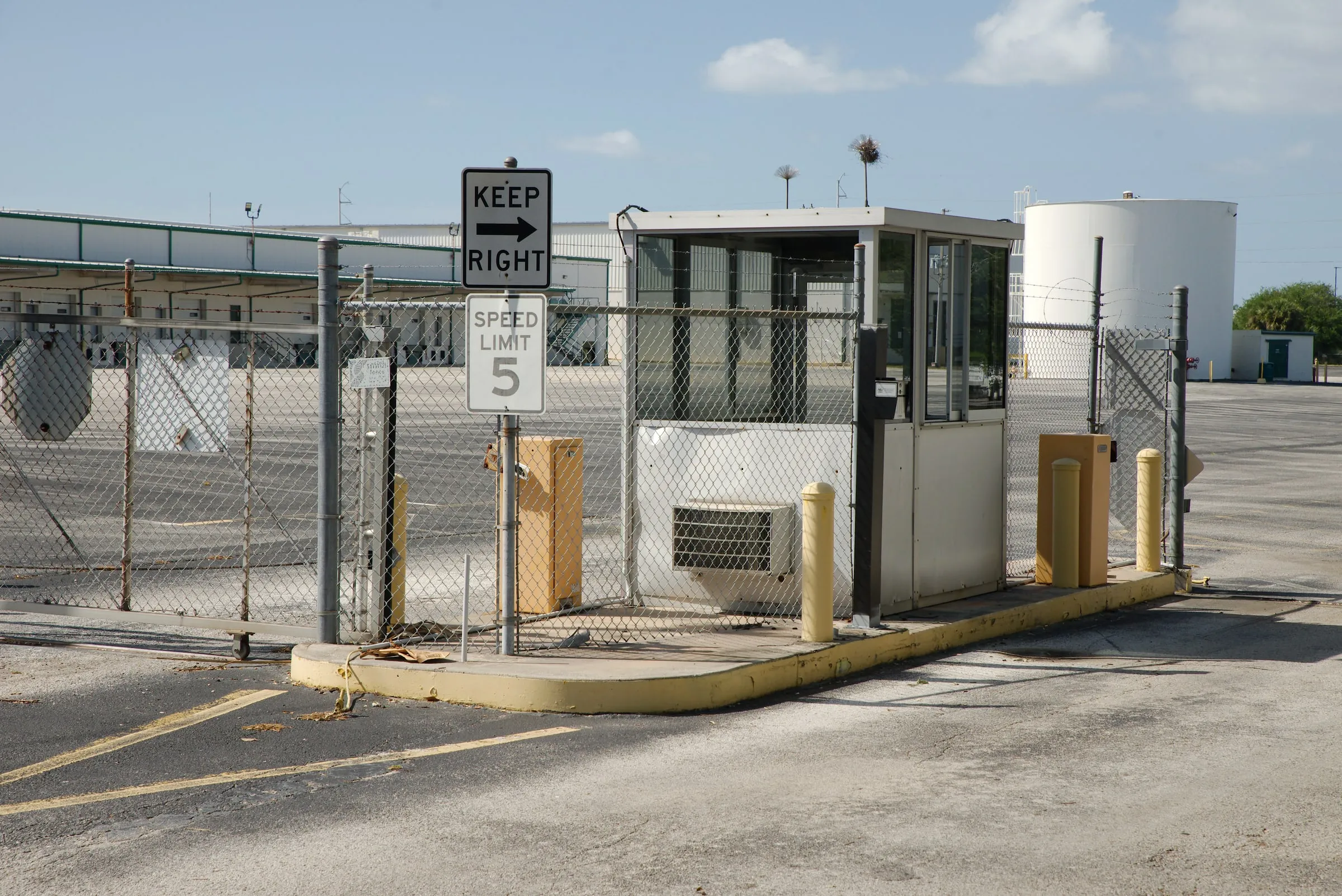 Fenced security checkpoint booth with a chain-link gate, Keep Right and Speed Limit 5 signs, at an industrial-style site entrance