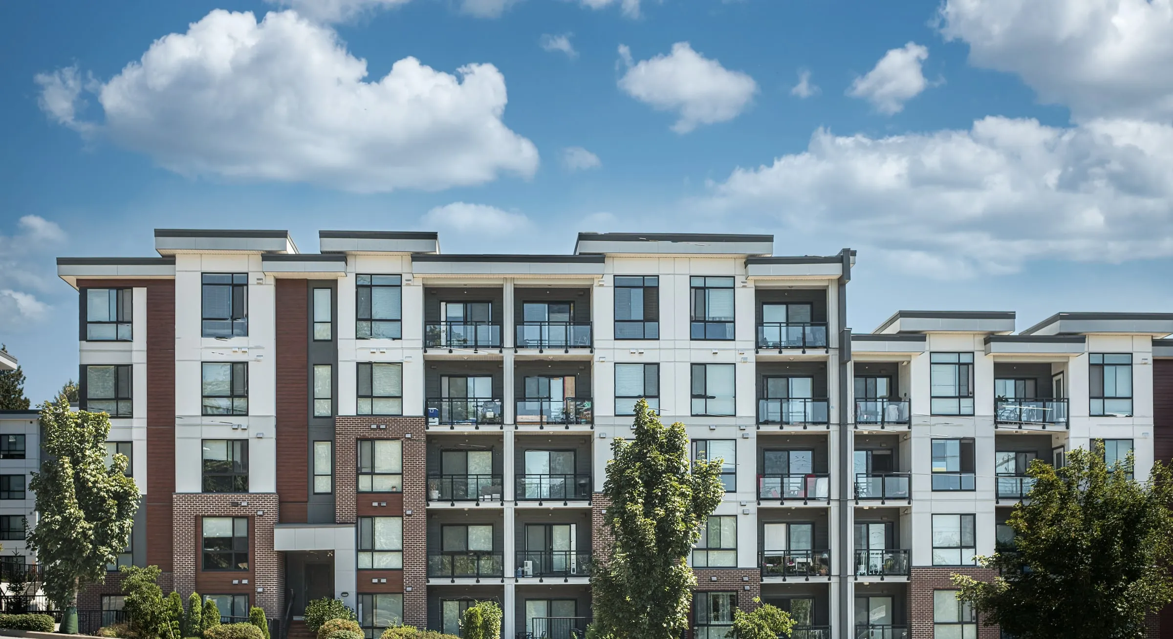 Five-story condominium building with brick and white panels, balconies and landscaped grounds