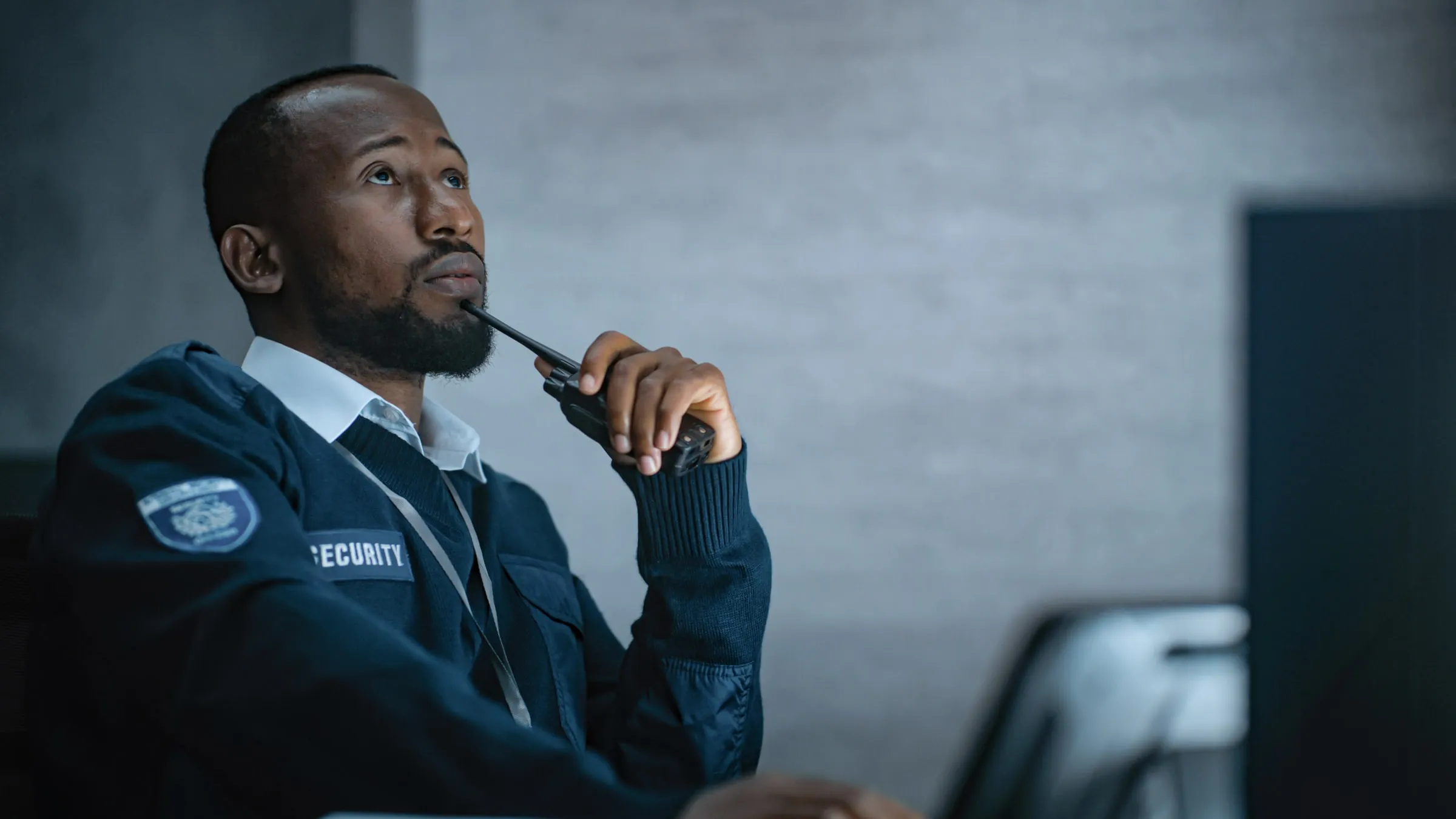 Security officer in a dark jacket holding a radio and looking up thoughtfully at a desk