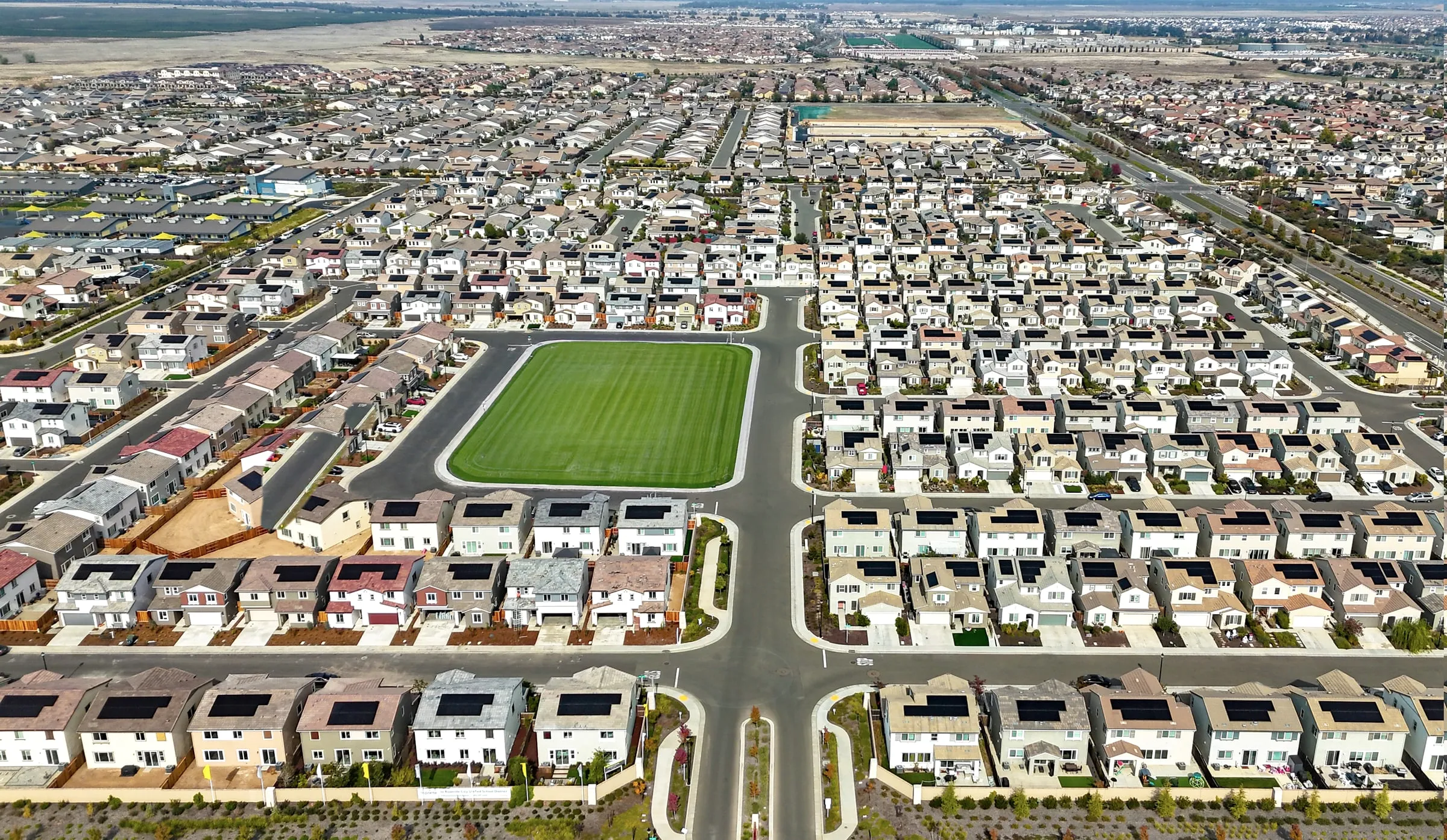 Aerial view of a large master-planned subdivision with rows of houses around a green park and a community pool