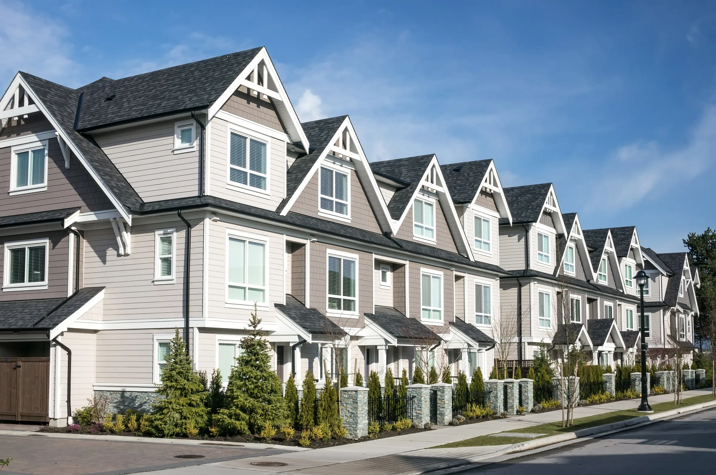 Row of three-story townhomes with gabled roofs, stone bases and small front lawns along a sidewalk
