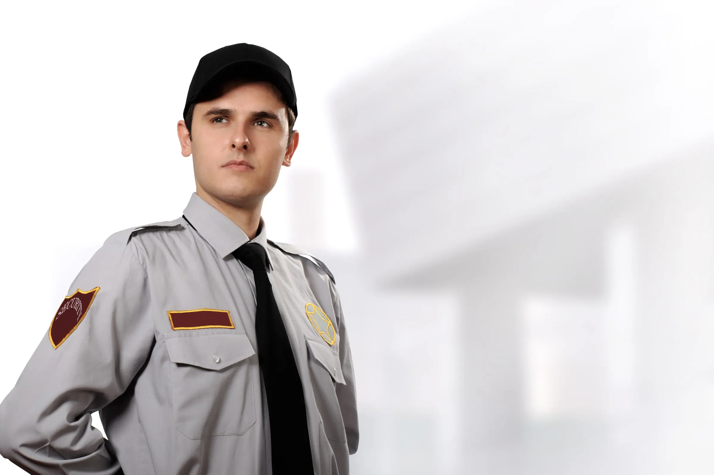 Security officer in a grey uniform shirt, tie and cap standing with a hand on his belt