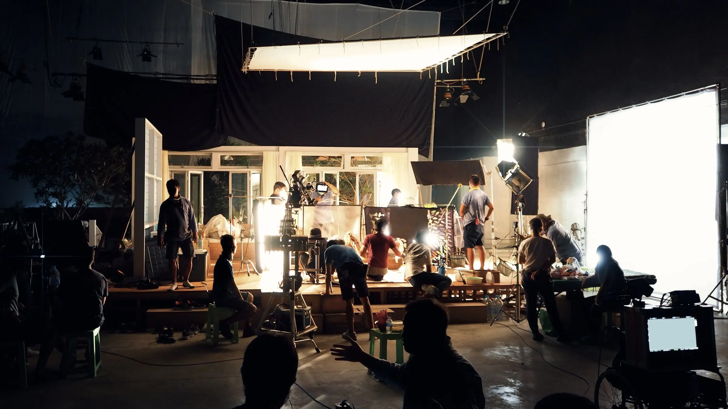 Film crew working on a lit set with lights, stands and a backdrop in a dark studio