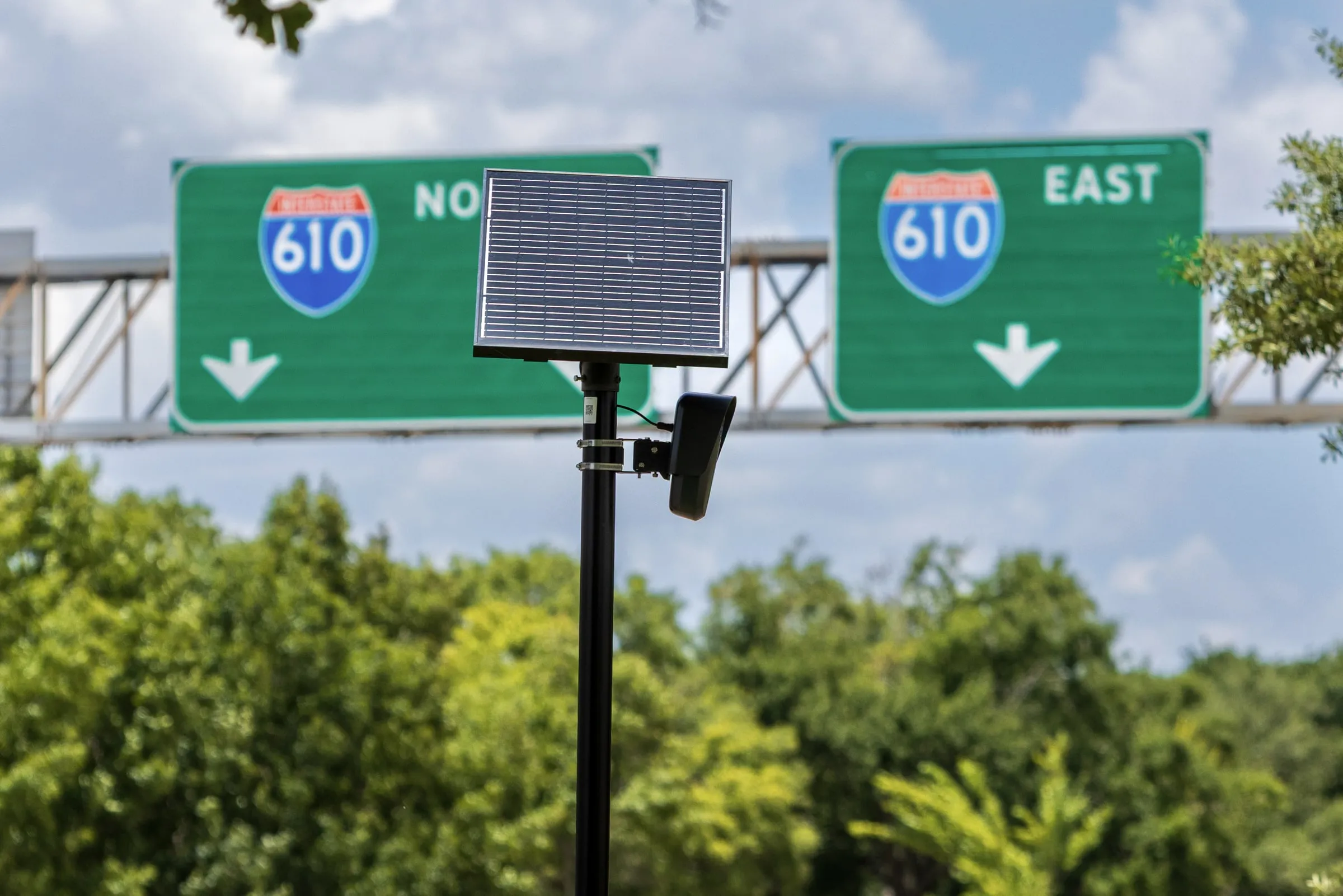 Green 610 freeway signs on a gantry above trees under a cloudy sky