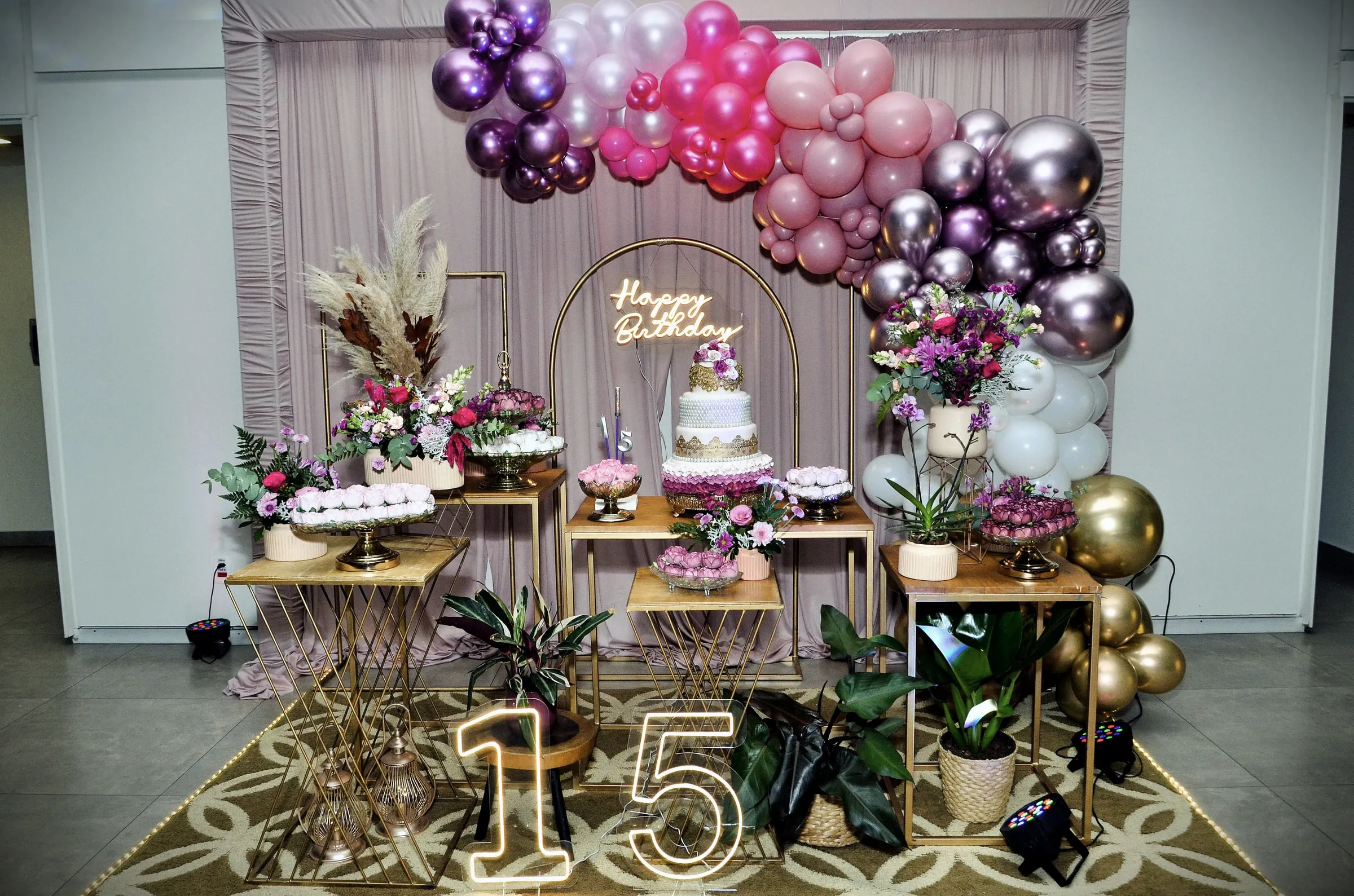 Quinceañera dessert table with a tiered cake, balloons in pink and gold and a large 15 sign