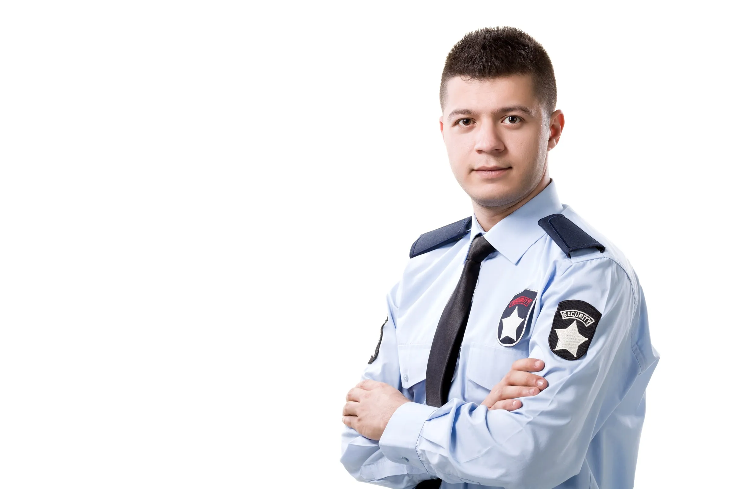 Young security officer in a light blue uniform shirt with SECURITY shoulder patches and a dark tie, arms folded, against a plain white background