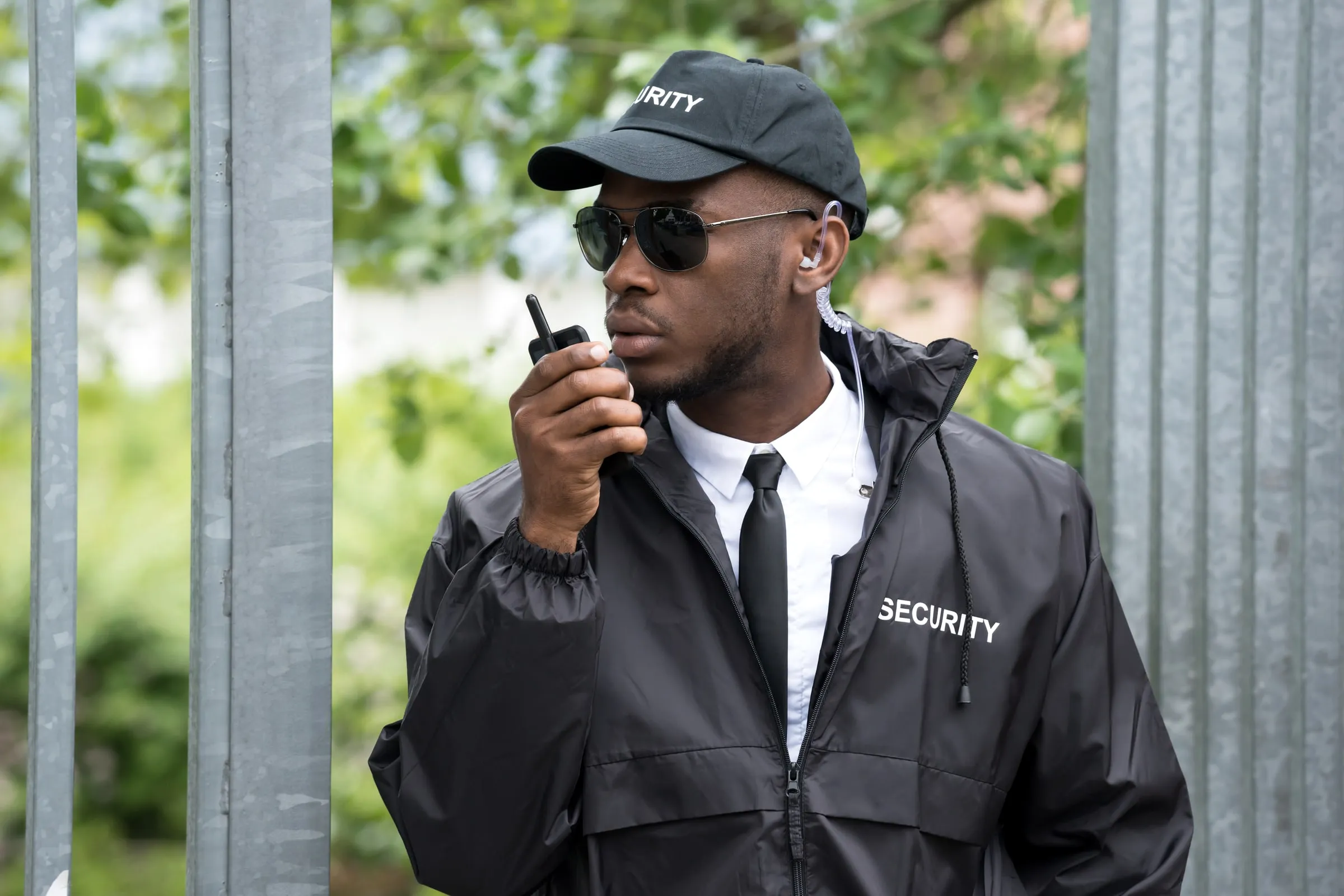 Security officer in a black cap and jacket speaking into a radio outdoors