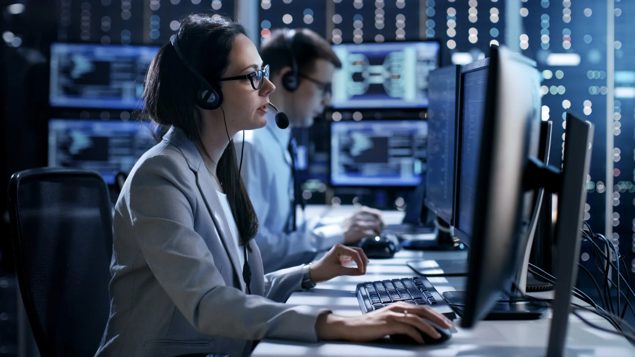 Two operators with headsets working at monitors in a dim control room