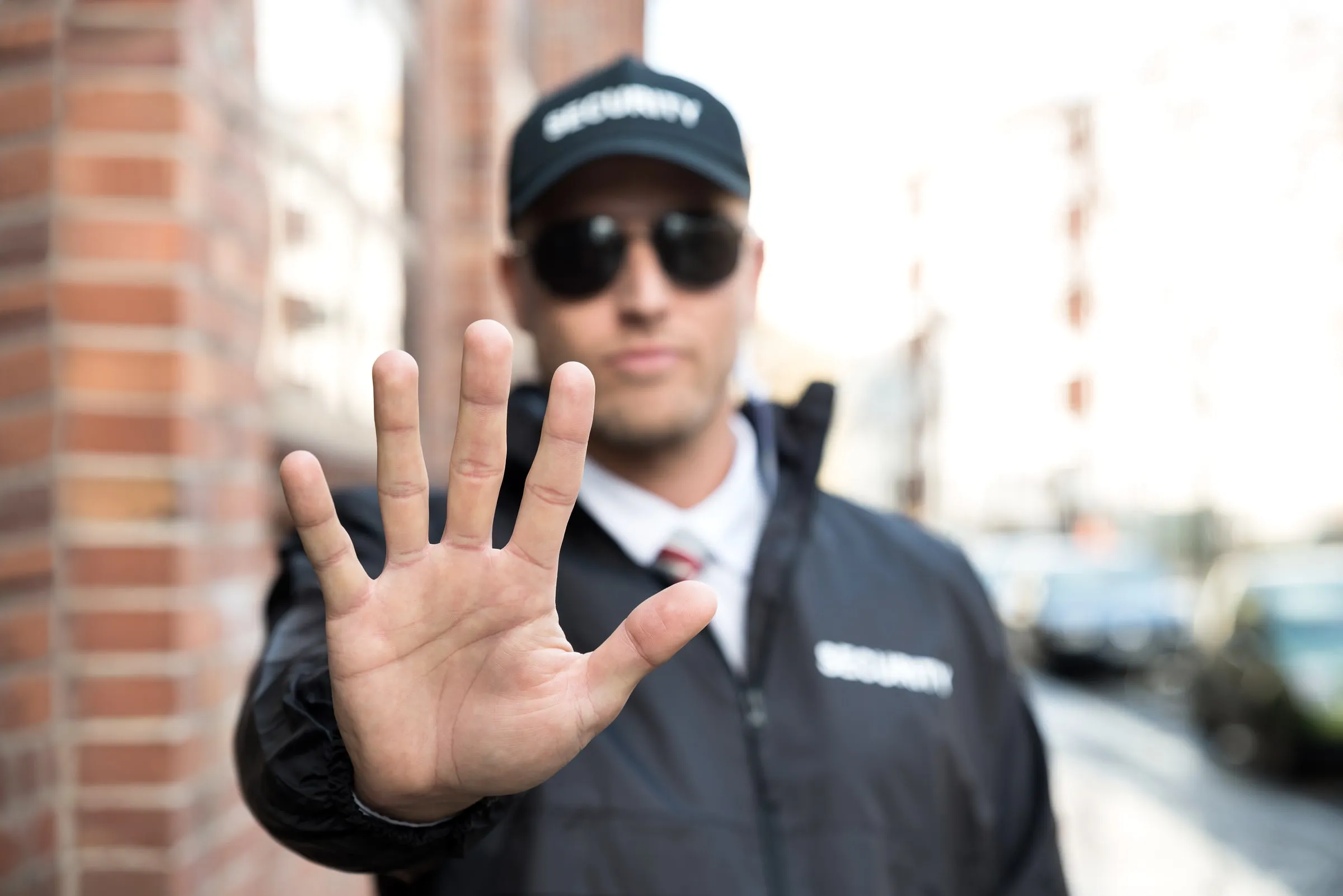 Uniformed security officer standing with hand raised in a stop gesture toward the camera on a city street