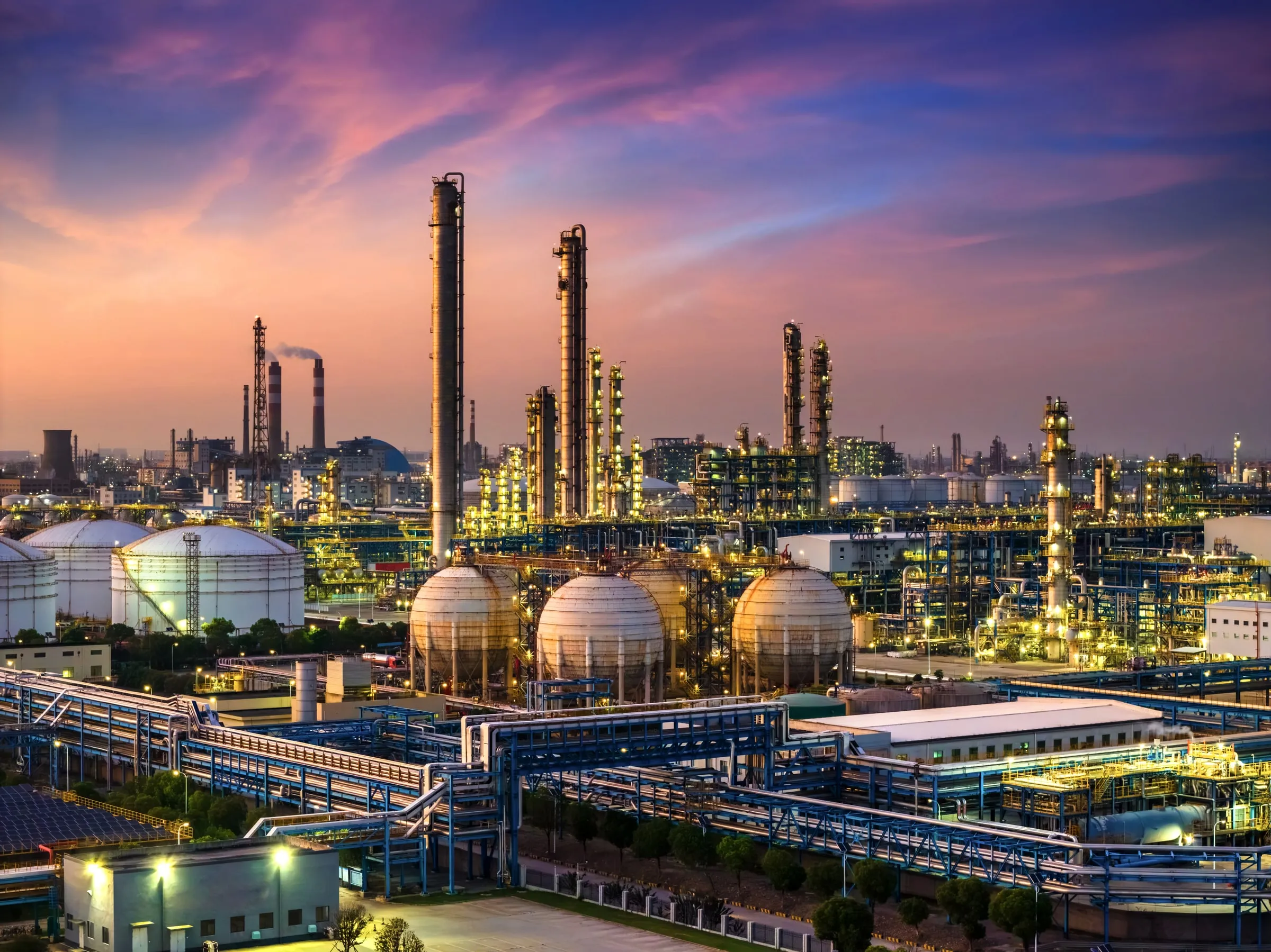 Chemical plant or refinery at dusk with illuminated distillation towers, spherical storage tanks and connecting pipe racks