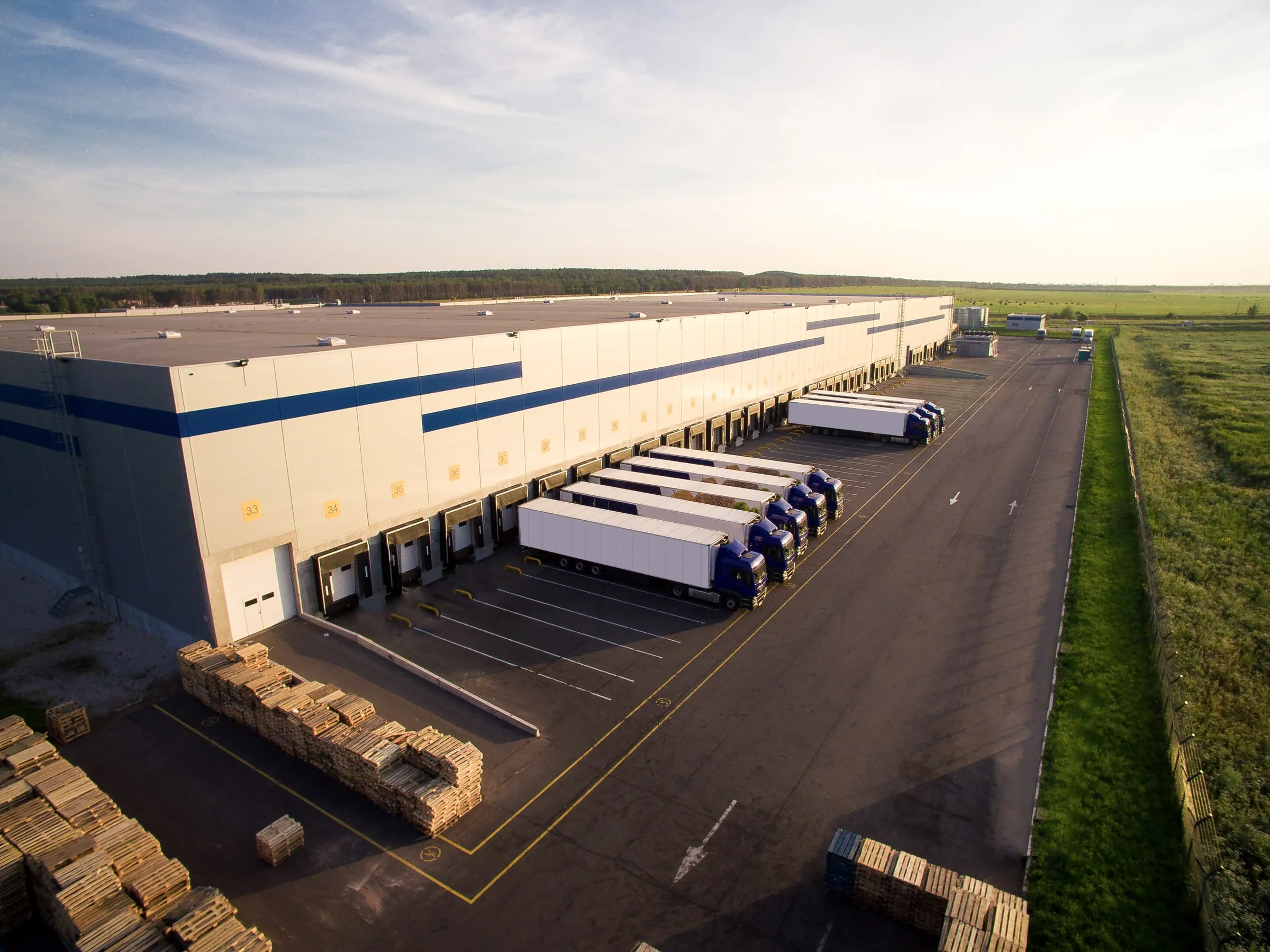Aerial view of a large distribution center with dozens of loading dock doors and trailers backed in along the building
