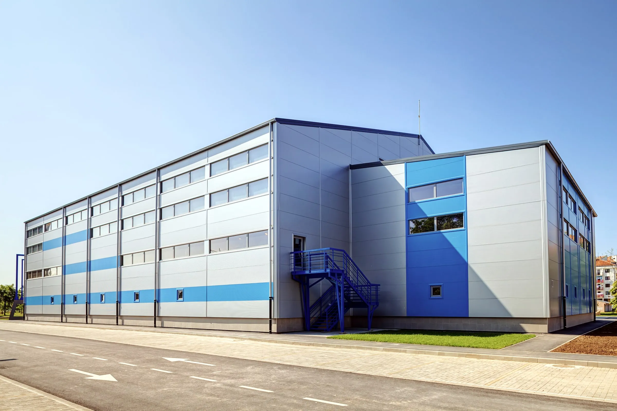 Multi-story industrial building with metal cladding, exterior stairwell and loading area under a clear sky