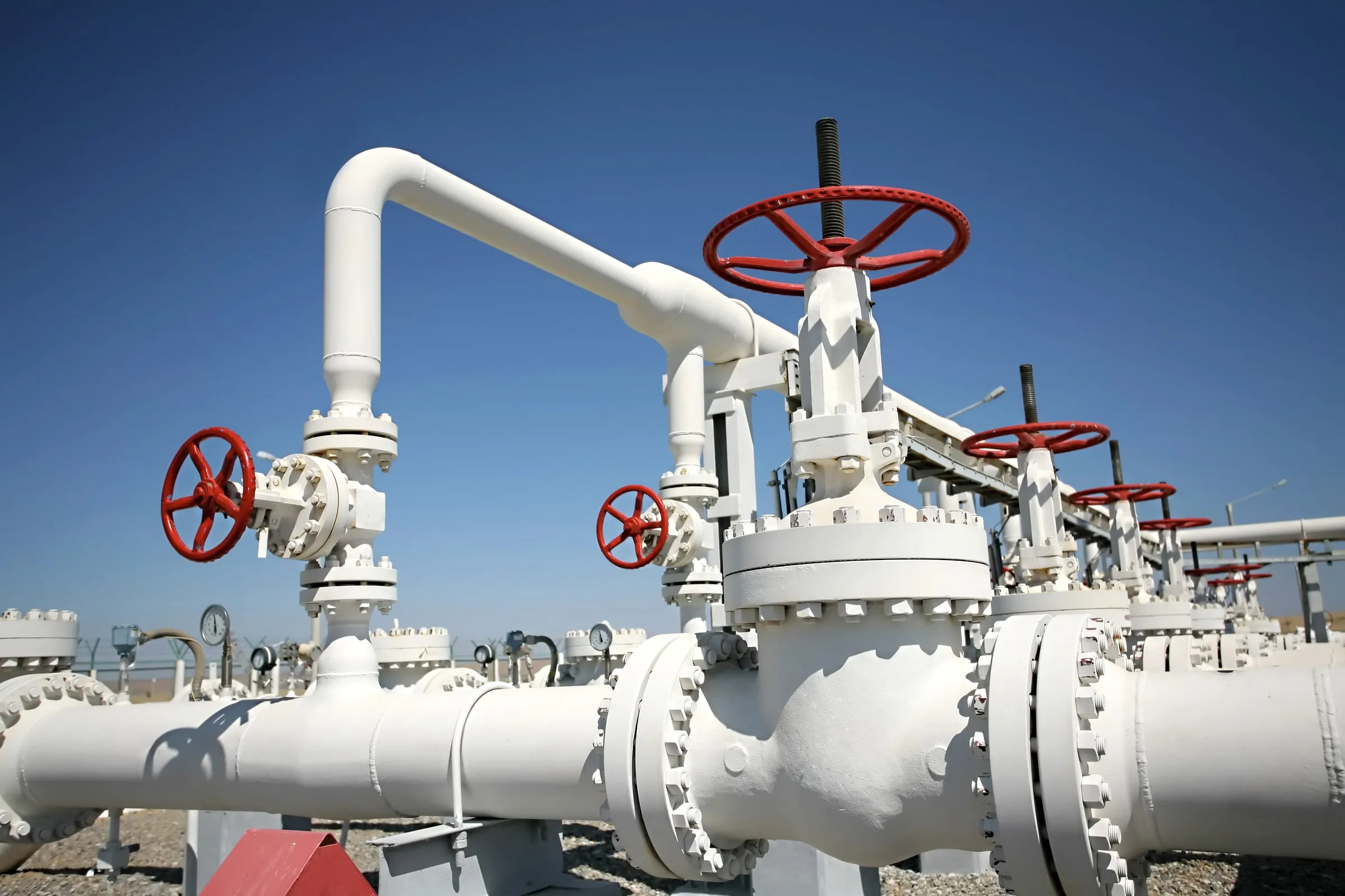 Close-up of red-handled valve wheels and white piping at an oil and gas production facility