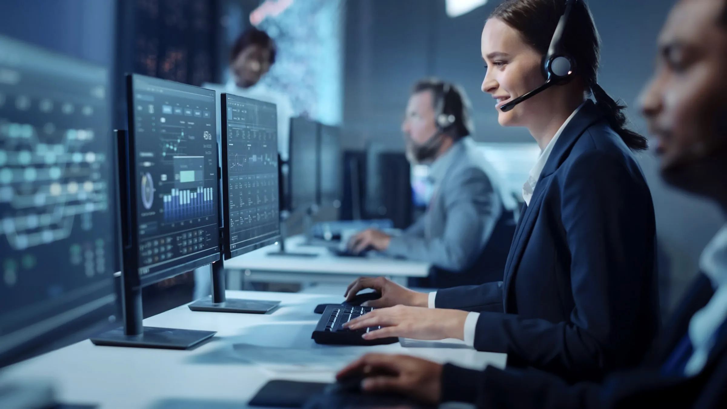 Dispatch operators wearing headsets working at a row of computer monitors displaying data and charts in a control room