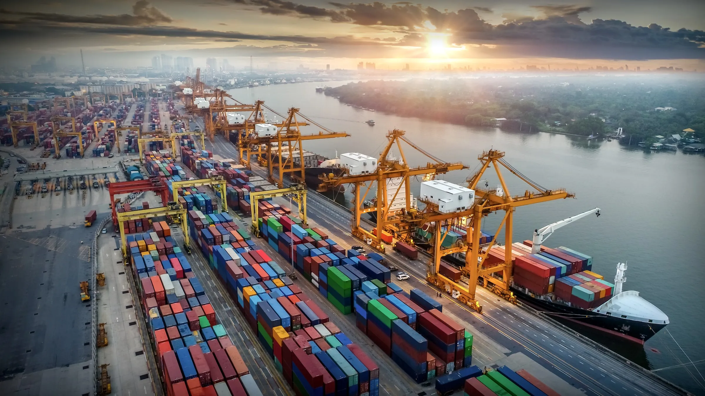 Aerial view of a container port terminal at sunrise with gantry cranes, stacked shipping containers and a docked cargo ship