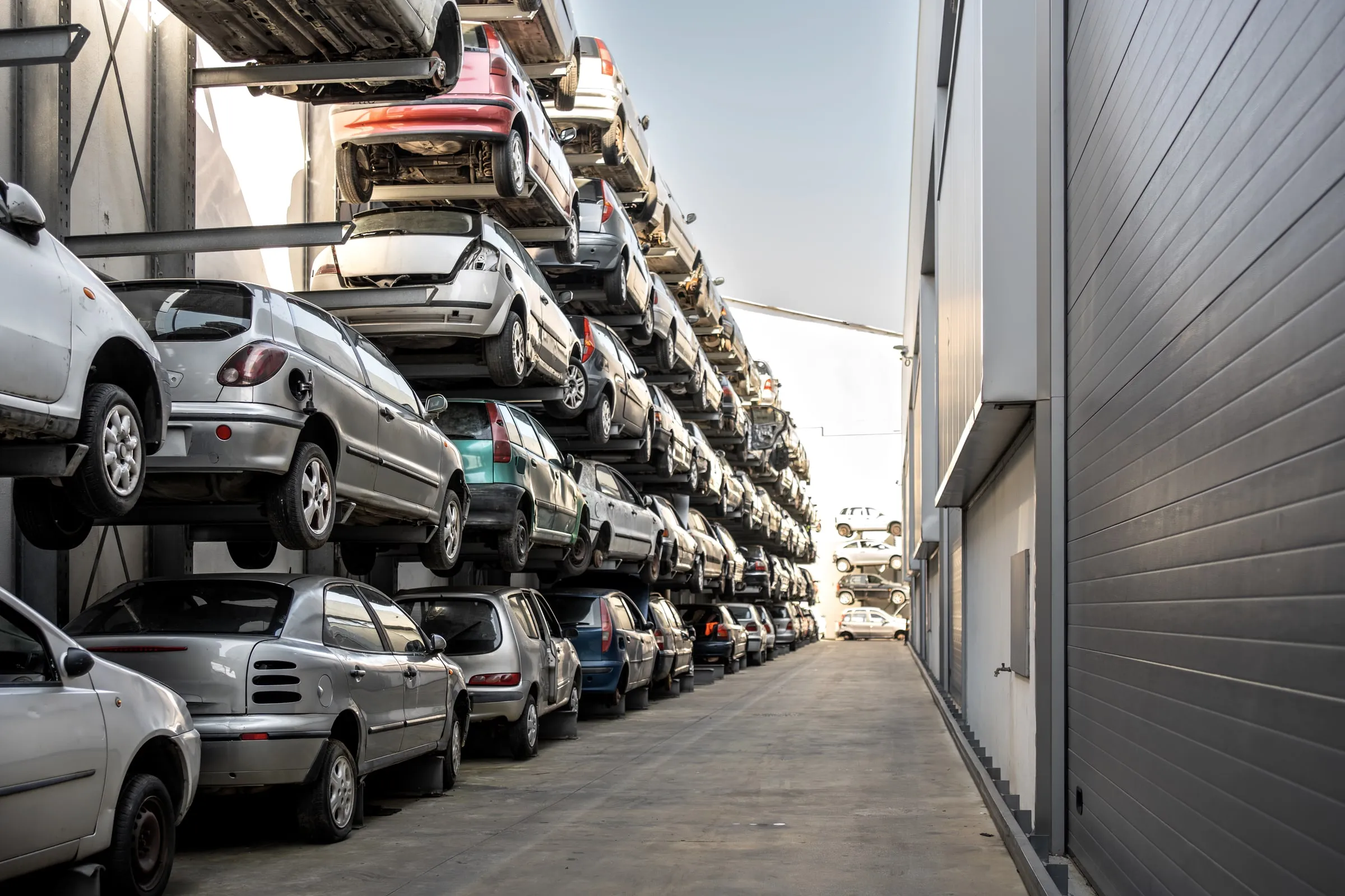 Rows of stacked wrecked and salvaged cars stored on multi-level racks in an outdoor auto salvage yard
