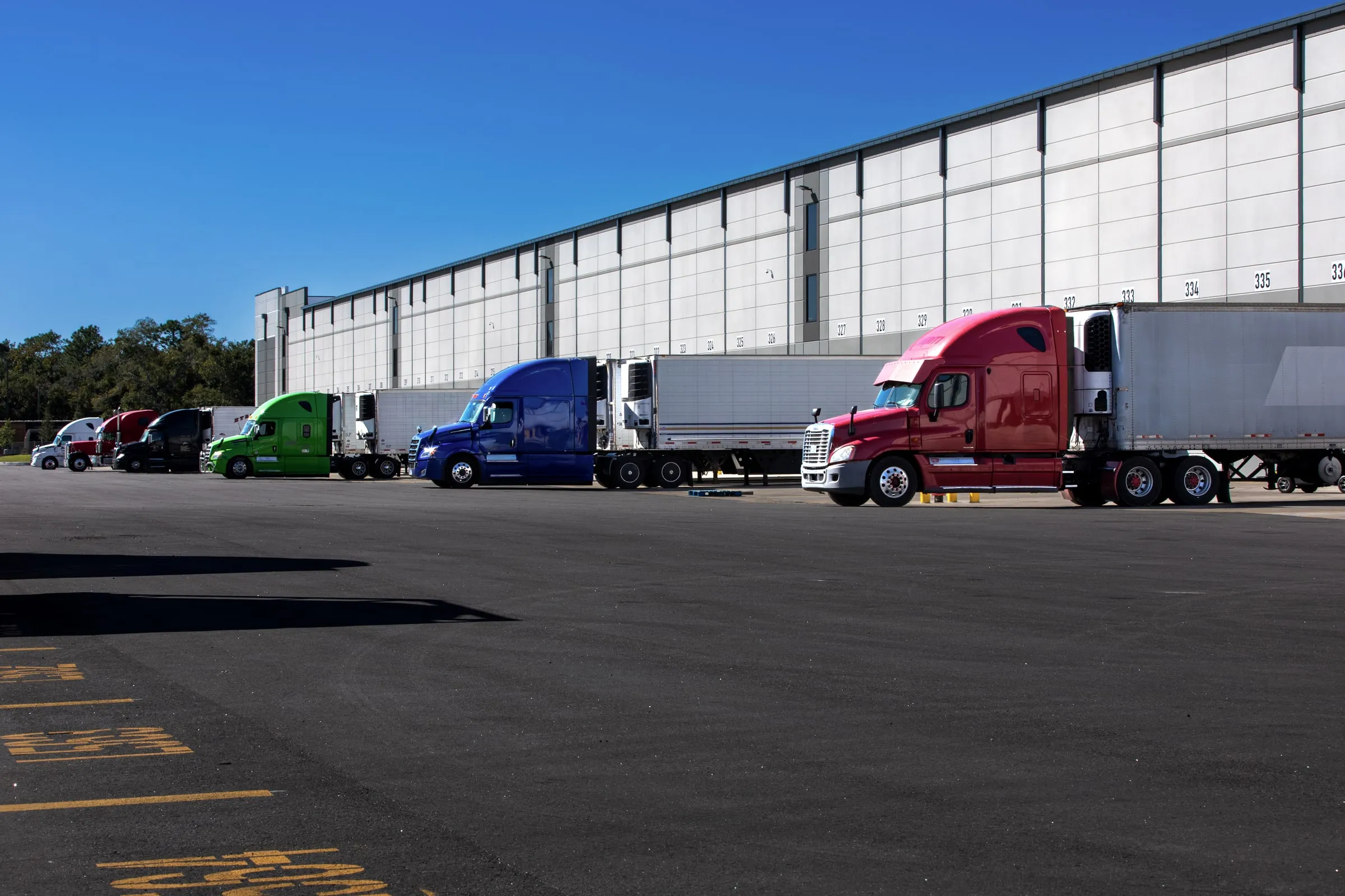 Rows of tractor-trailers backed into loading dock doors along a long warehouse building under a clear sky