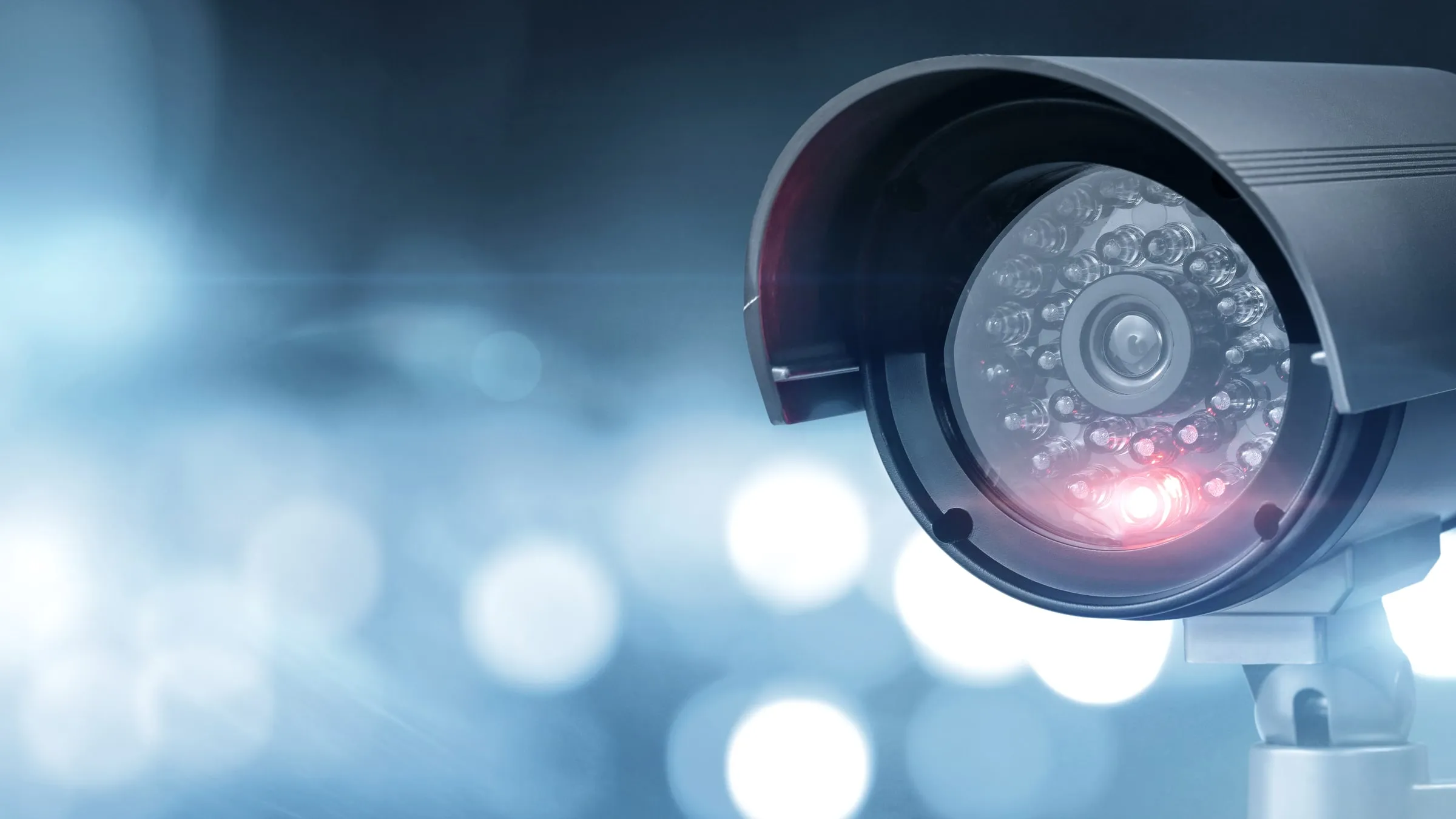 Dome security camera with a red indicator light against a bright bokeh background