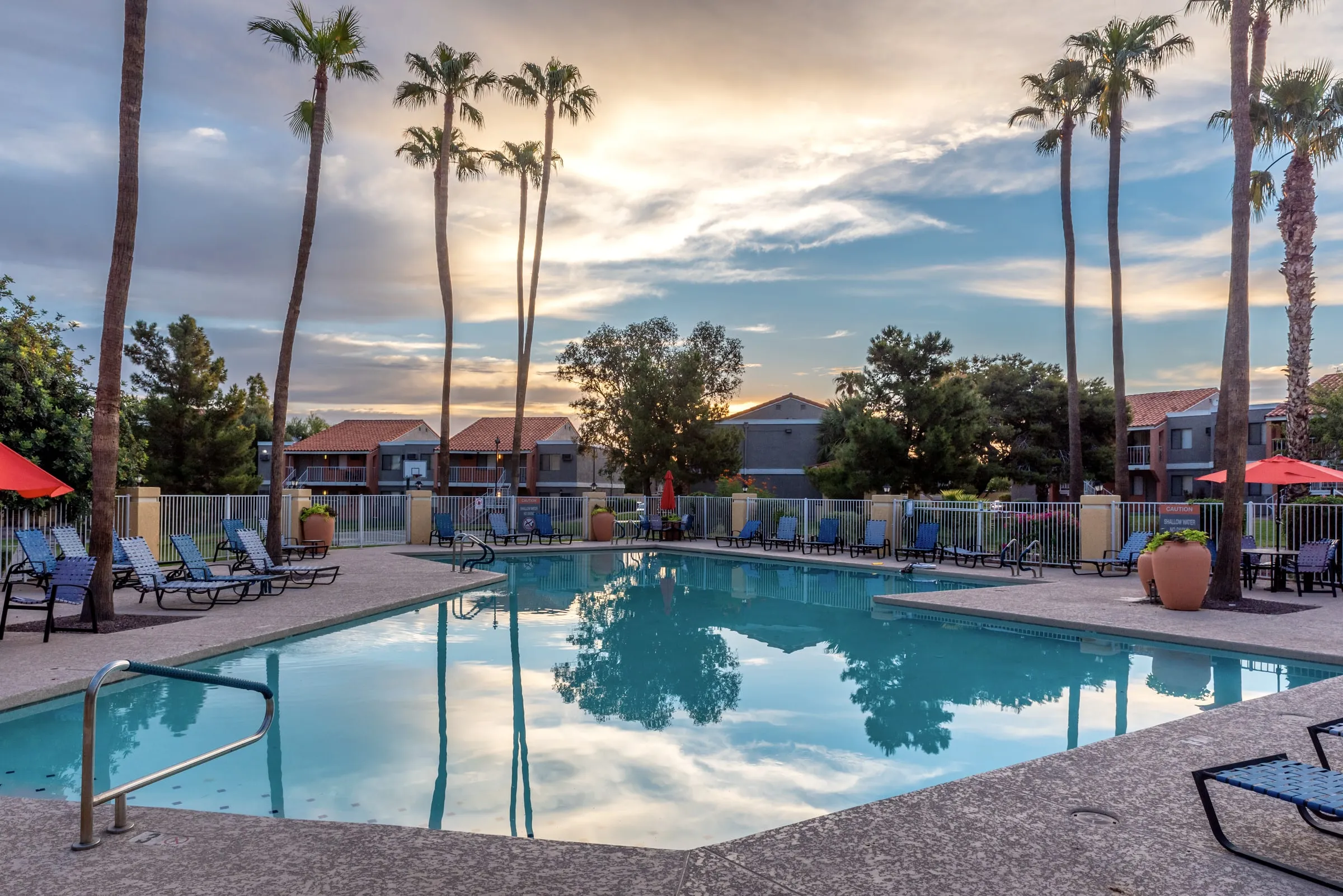 Apartment community swimming pool at dawn with palm trees, lounge chairs and two-storey buildings behind