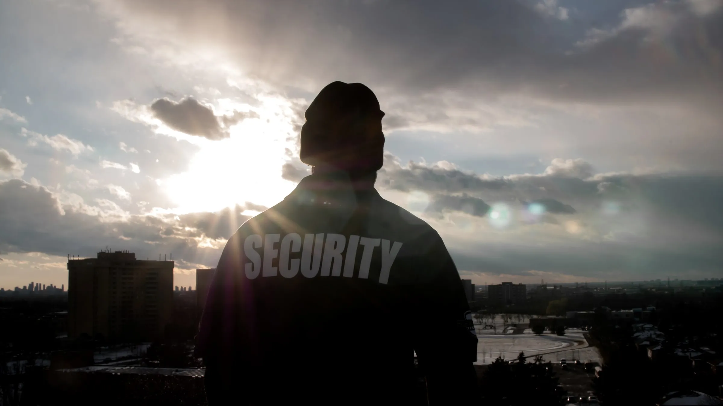 Silhouette of a security officer in a SECURITY jacket against a dramatic cloudy sky