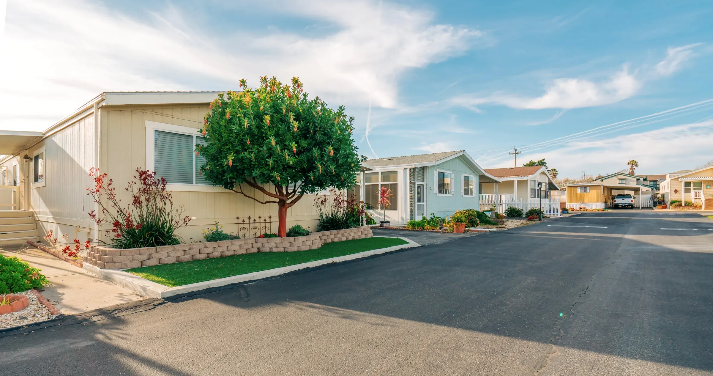 Street in a manufactured home community with neat homes, a tree and a carport