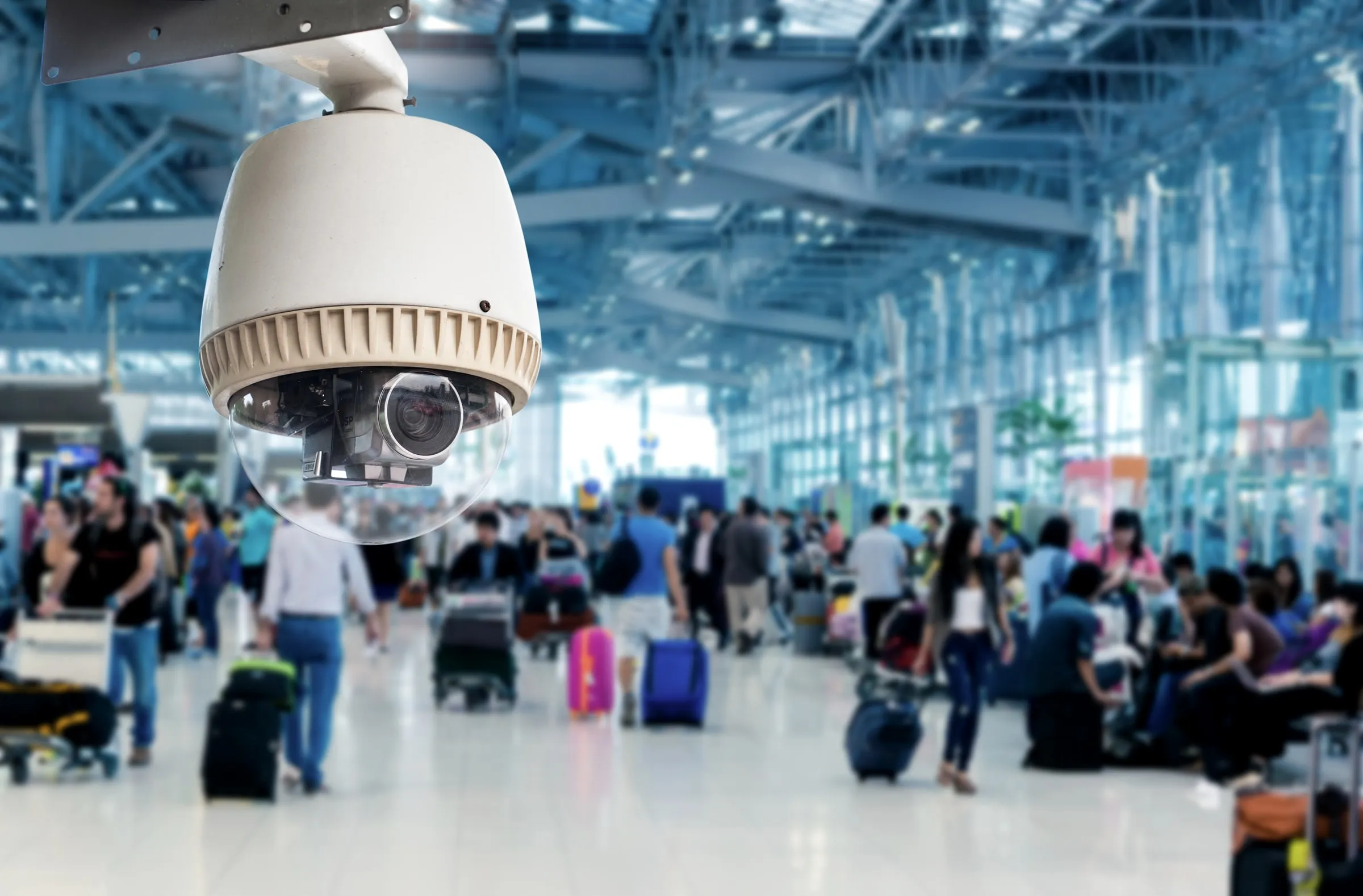Dome camera mounted high in a busy glass-roofed concourse full of people