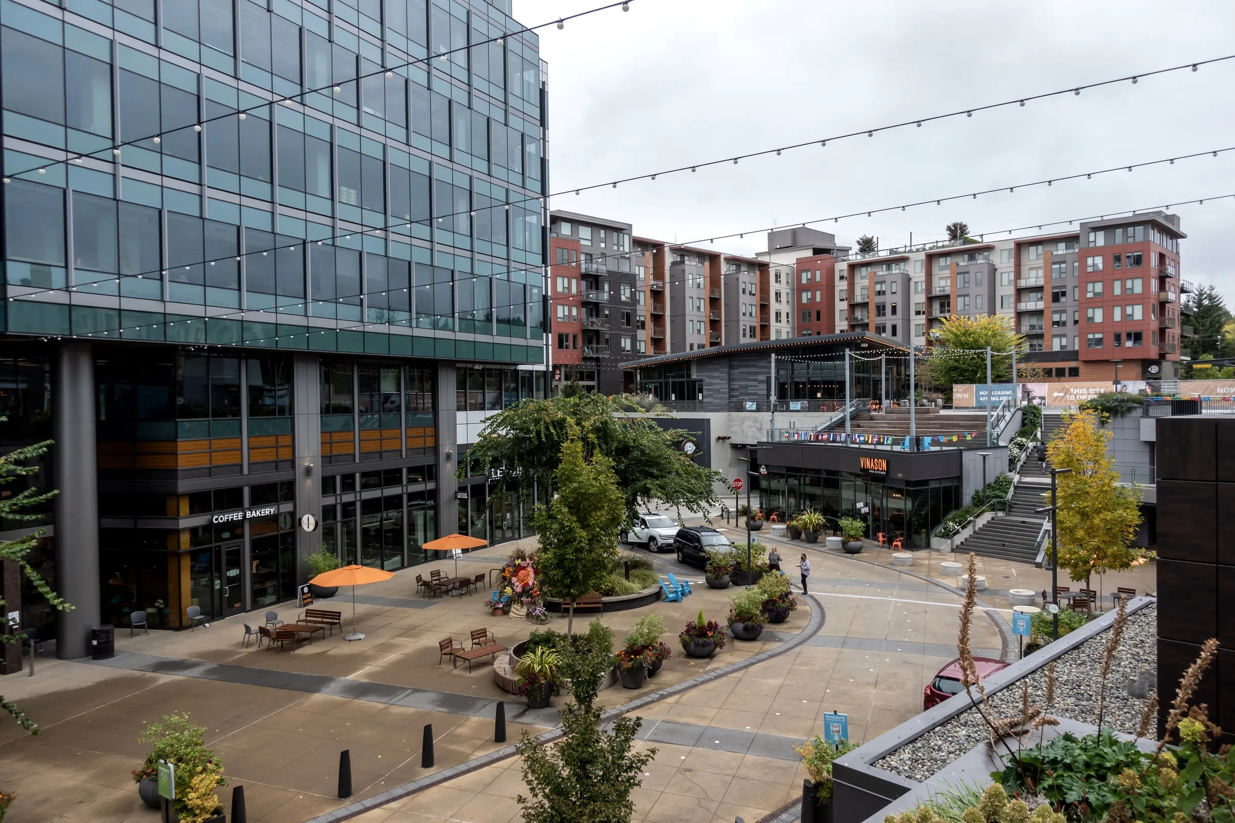 Mixed-use development with apartments above shops around a landscaped plaza with string lights