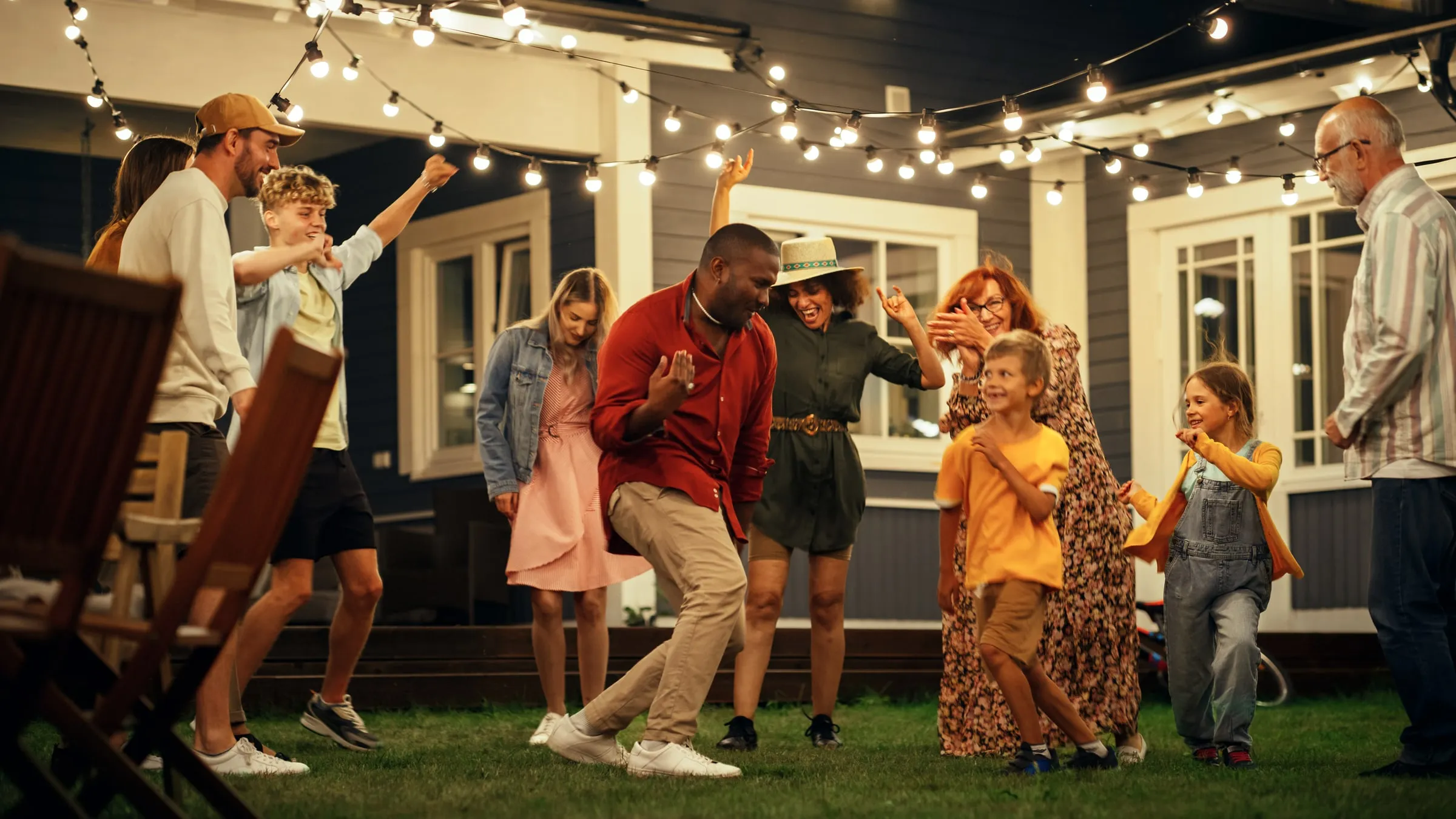 Residents dancing at an outdoor evening party under string lights beside a building
