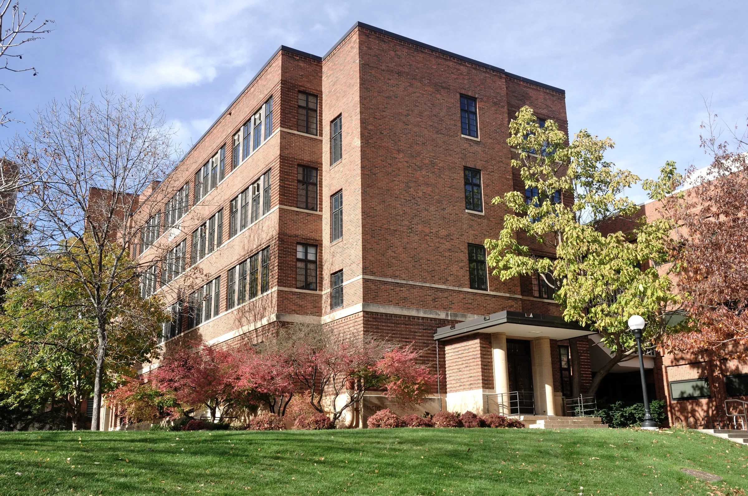 Four-storey red brick residence hall with a columned entrance on a university campus in autumn