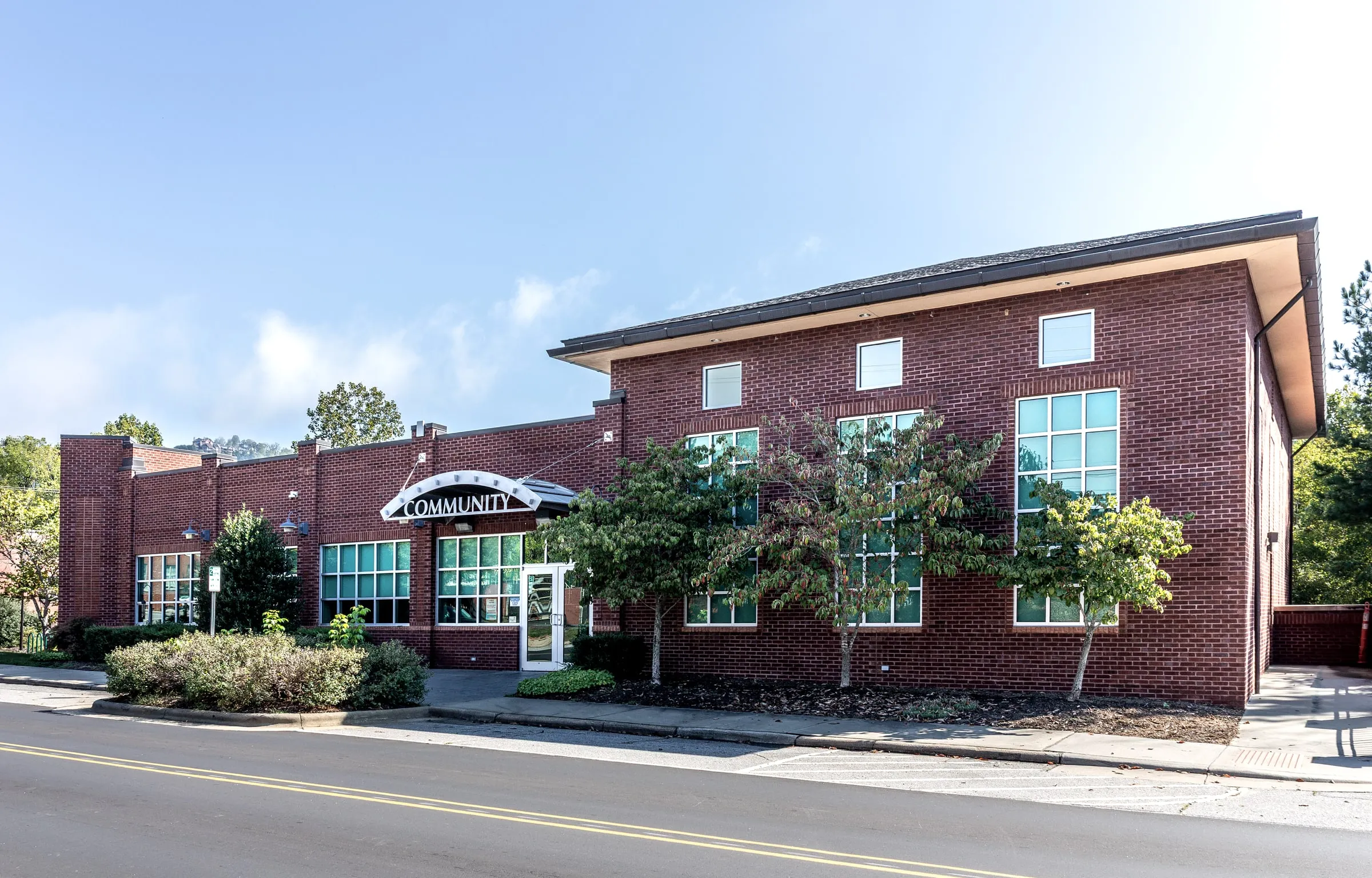 Brick community center with a peaked roof and glass entrance on a tree-lined street