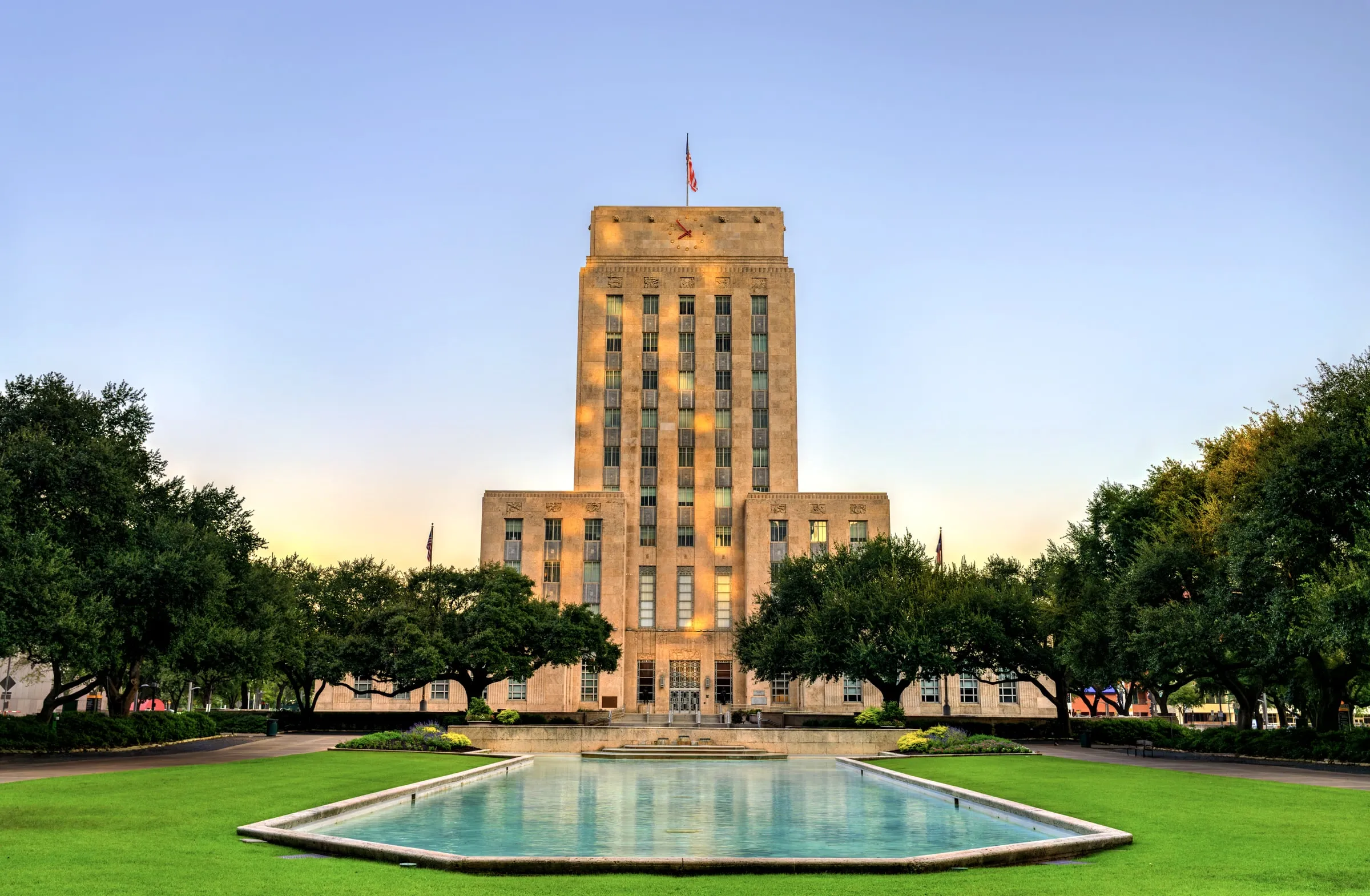 Houston City Hall and its reflecting pool at sunrise, framed by live oaks