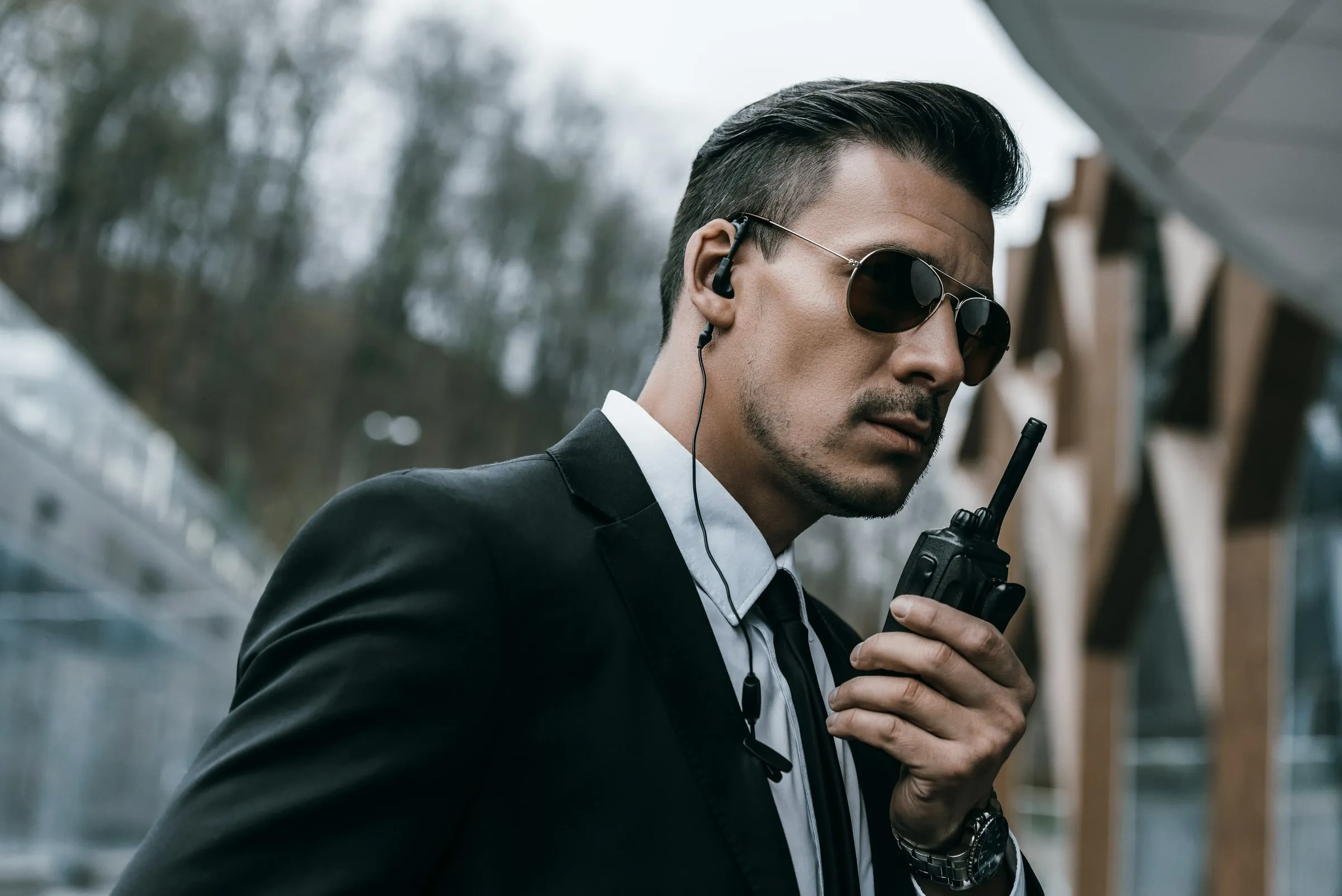 Security officer in a dark suit and sunglasses speaking into a radio with an earpiece