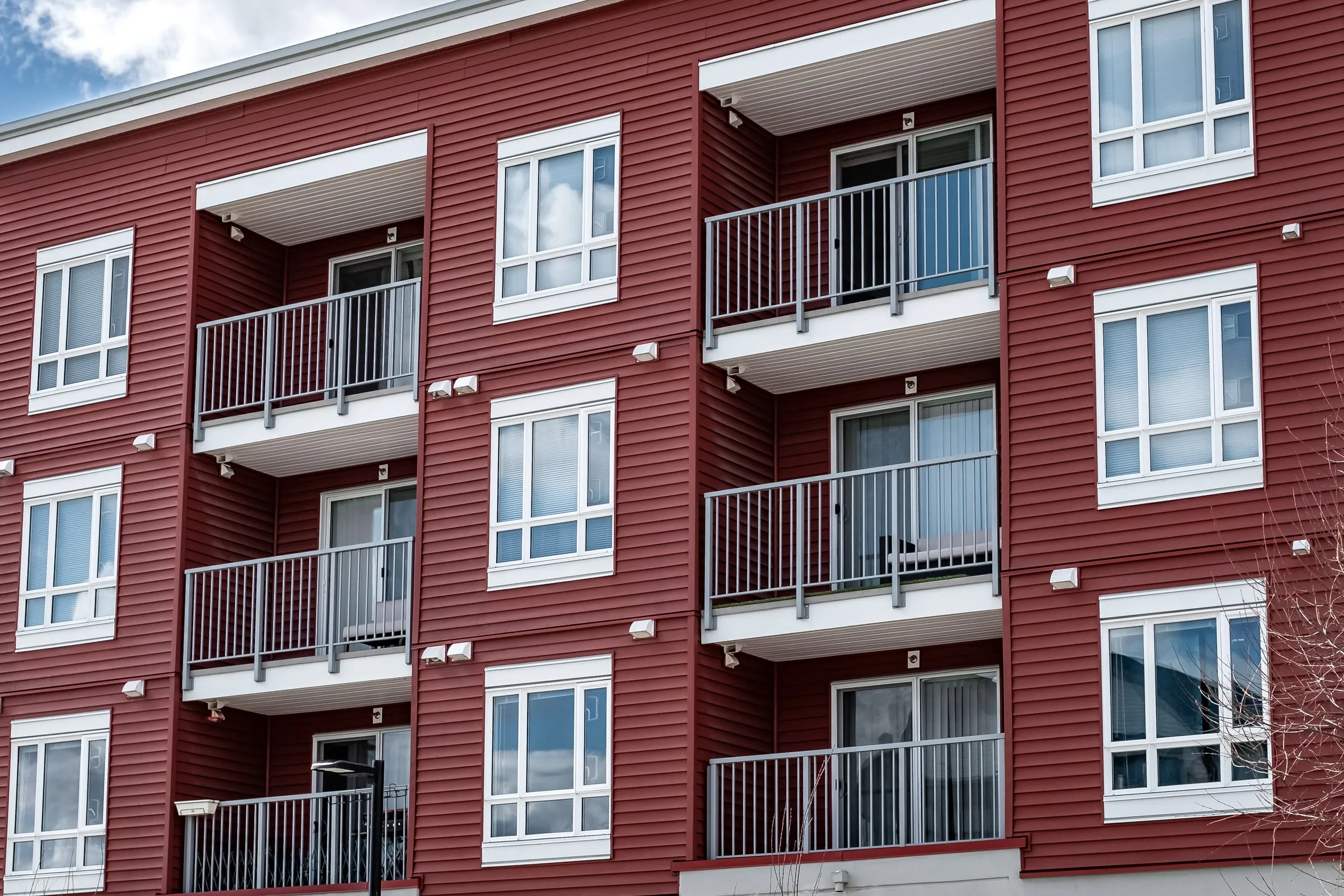 Red-brick apartment building with white balconies and railings against a blue sky