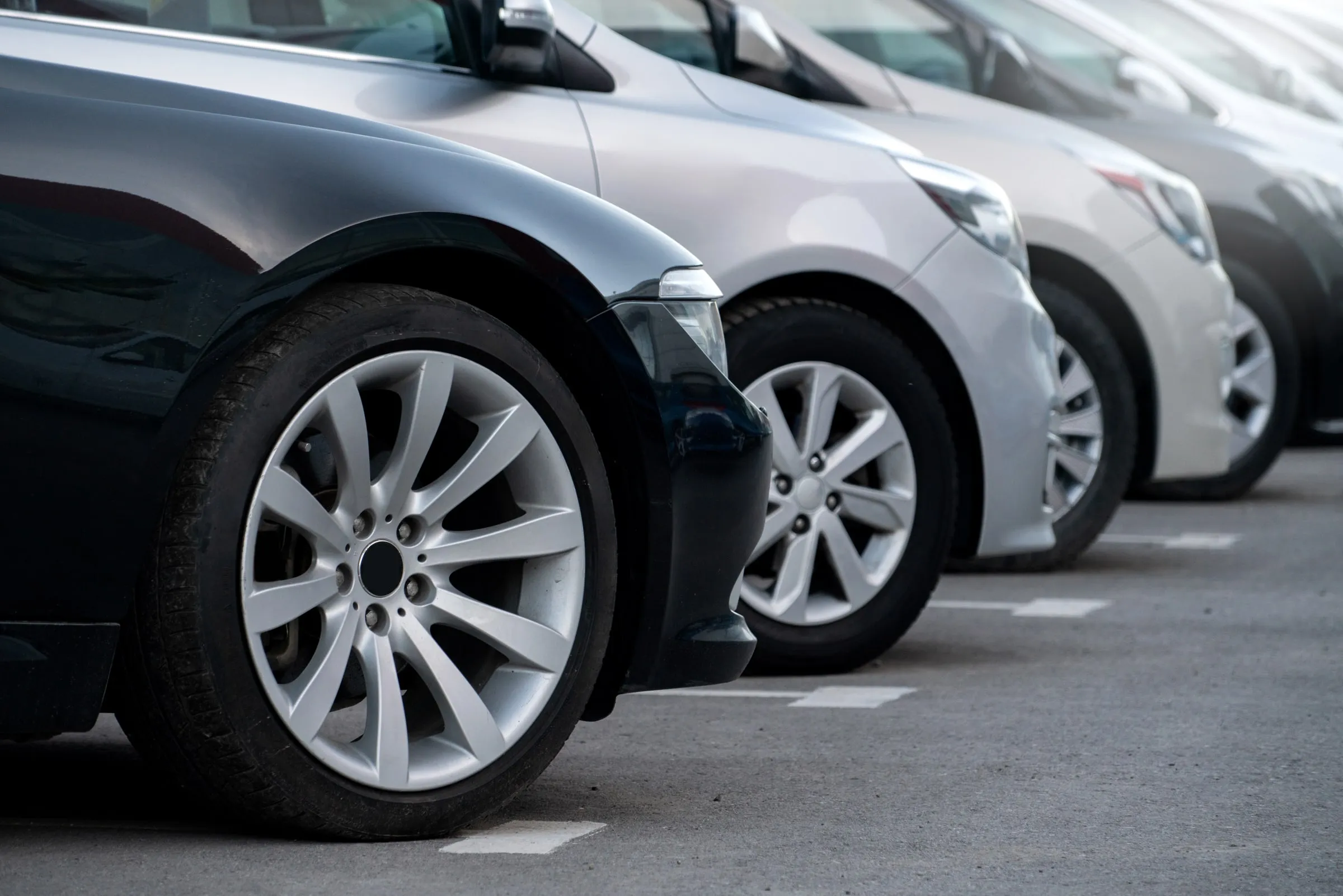 Close view of a row of parked cars in painted bays, the front wheel of a dark sedan nearest the camera