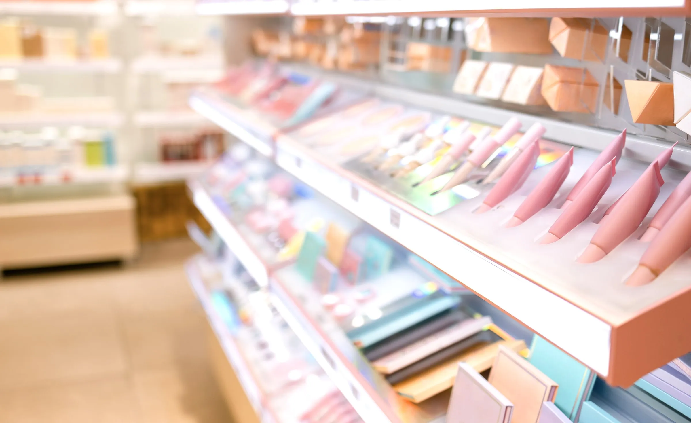 A softly blurred close-up of a cosmetics display shelf holding pink beauty tools and packaged products