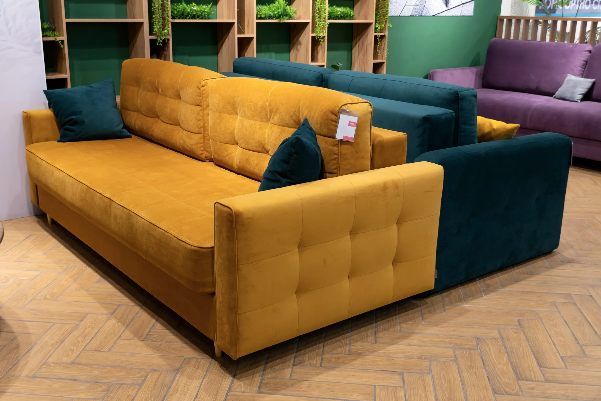 Furniture showroom with a mustard velvet sofa in front, teal and purple sofas behind it, on a herringbone wood floor