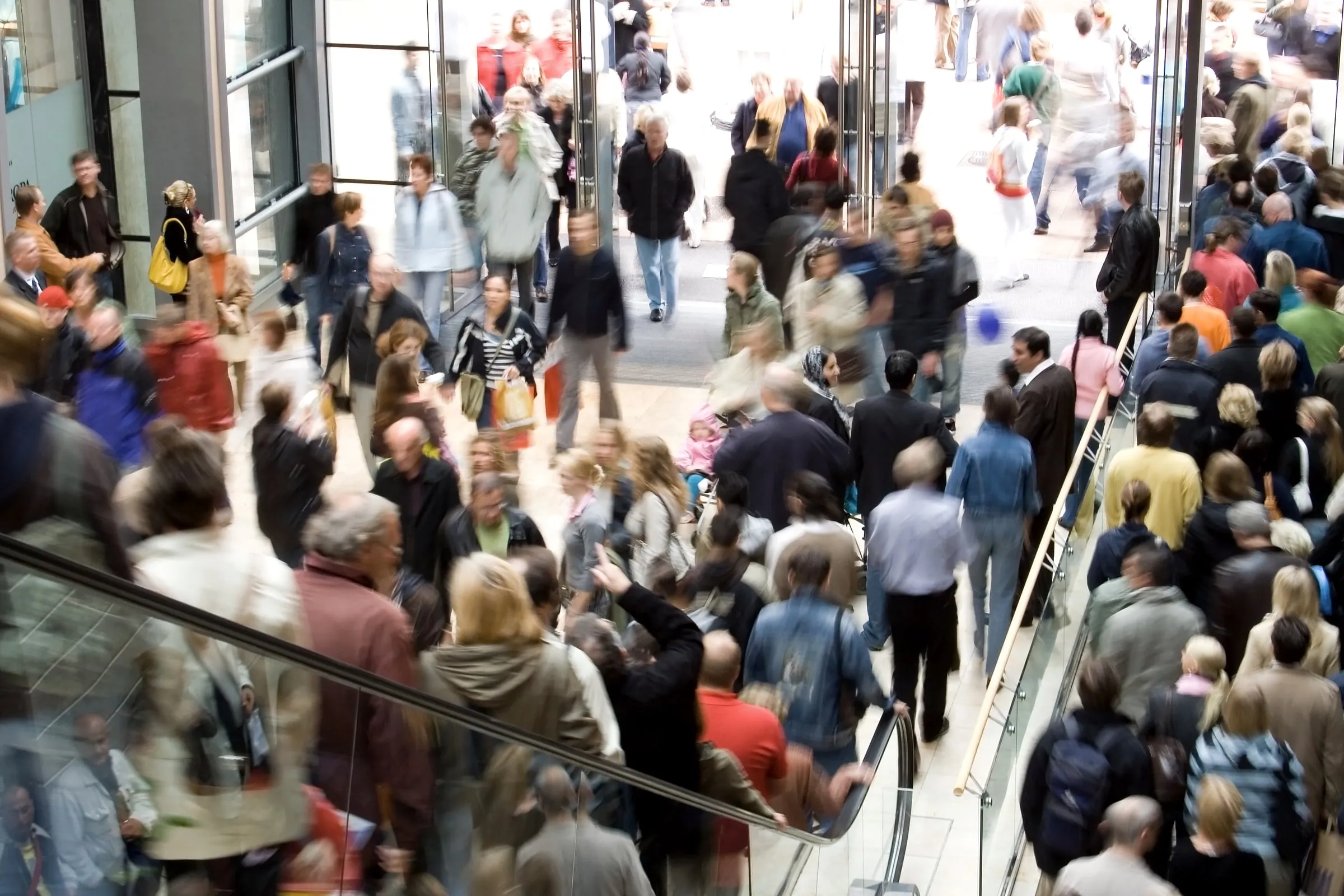 A crowded shopping center viewed from above, with many shoppers filling an escalator and walkway during a busy period