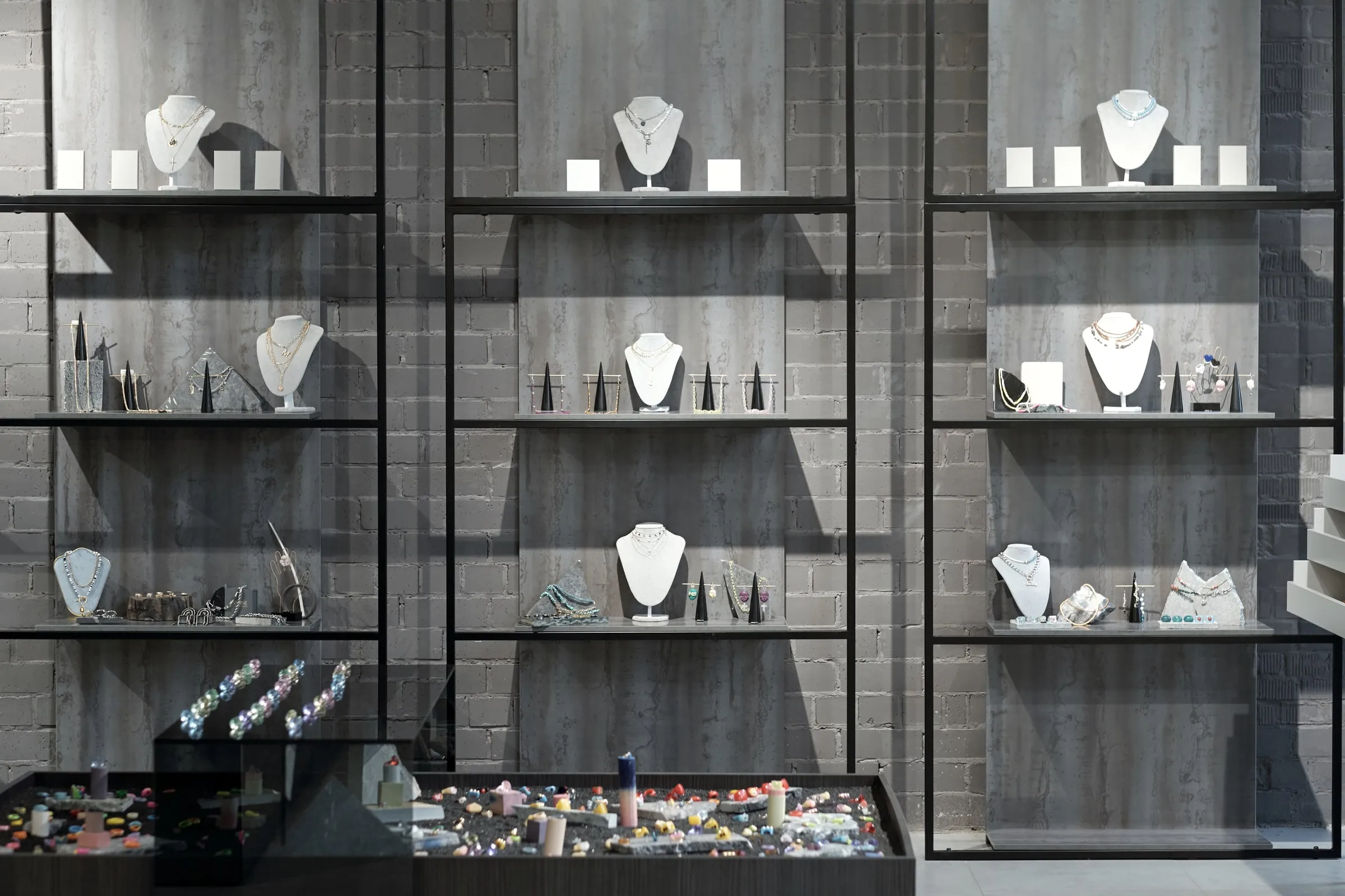 Glass display cases hold necklaces, bracelets and rings on mannequin busts against a concrete wall in a jewelry store