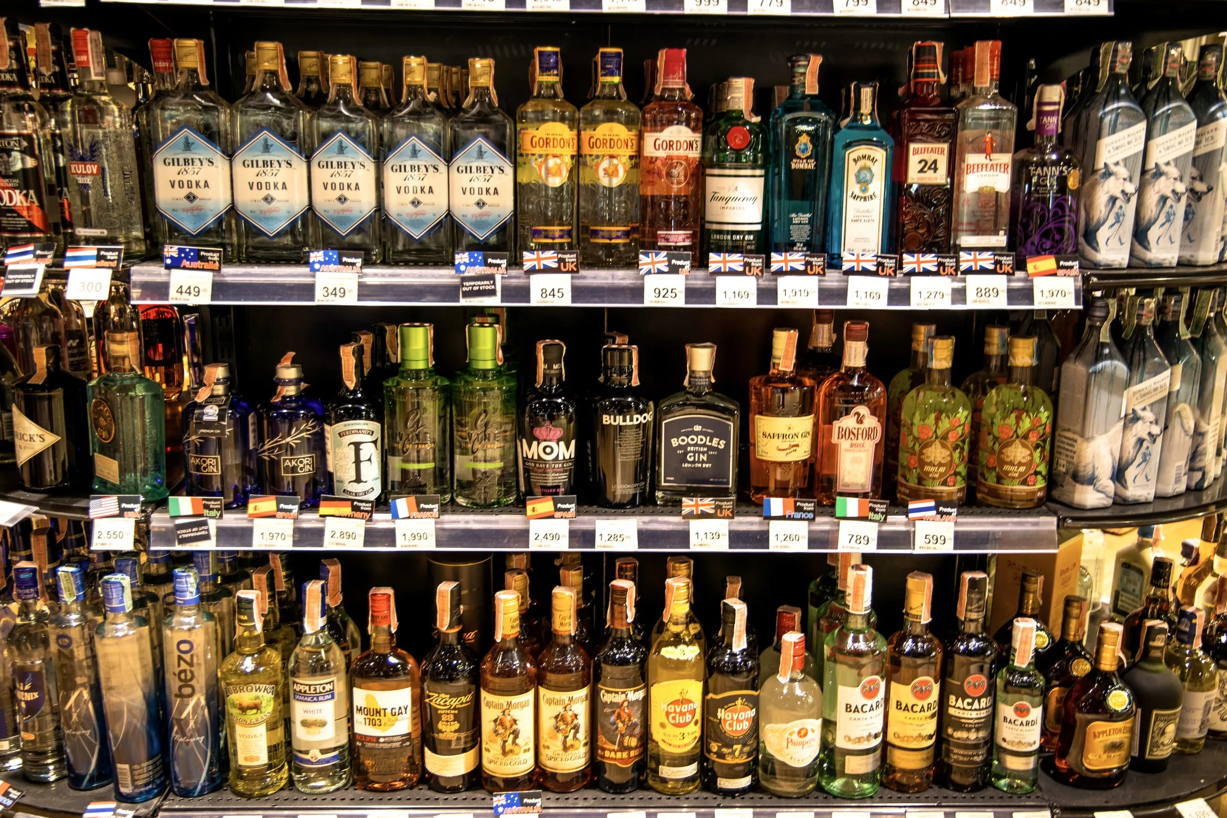 Shelves stocked with vodka, gin and rum bottles displaying price tags in a liquor store
