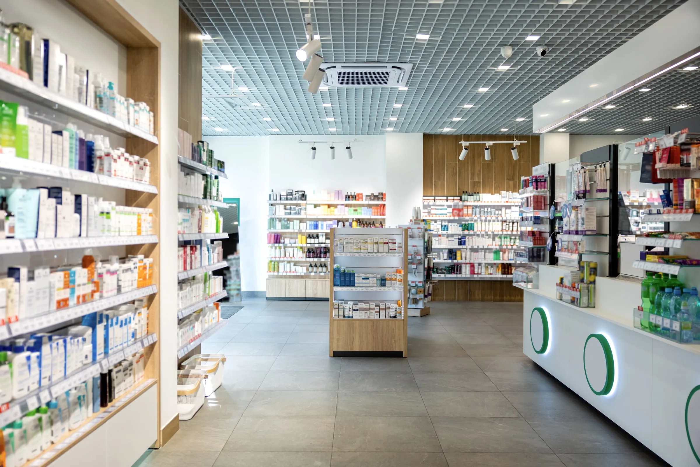 Aisles of a pharmacy sales floor lined with shelves of over-the-counter medicine and personal care products under an open grid ceiling