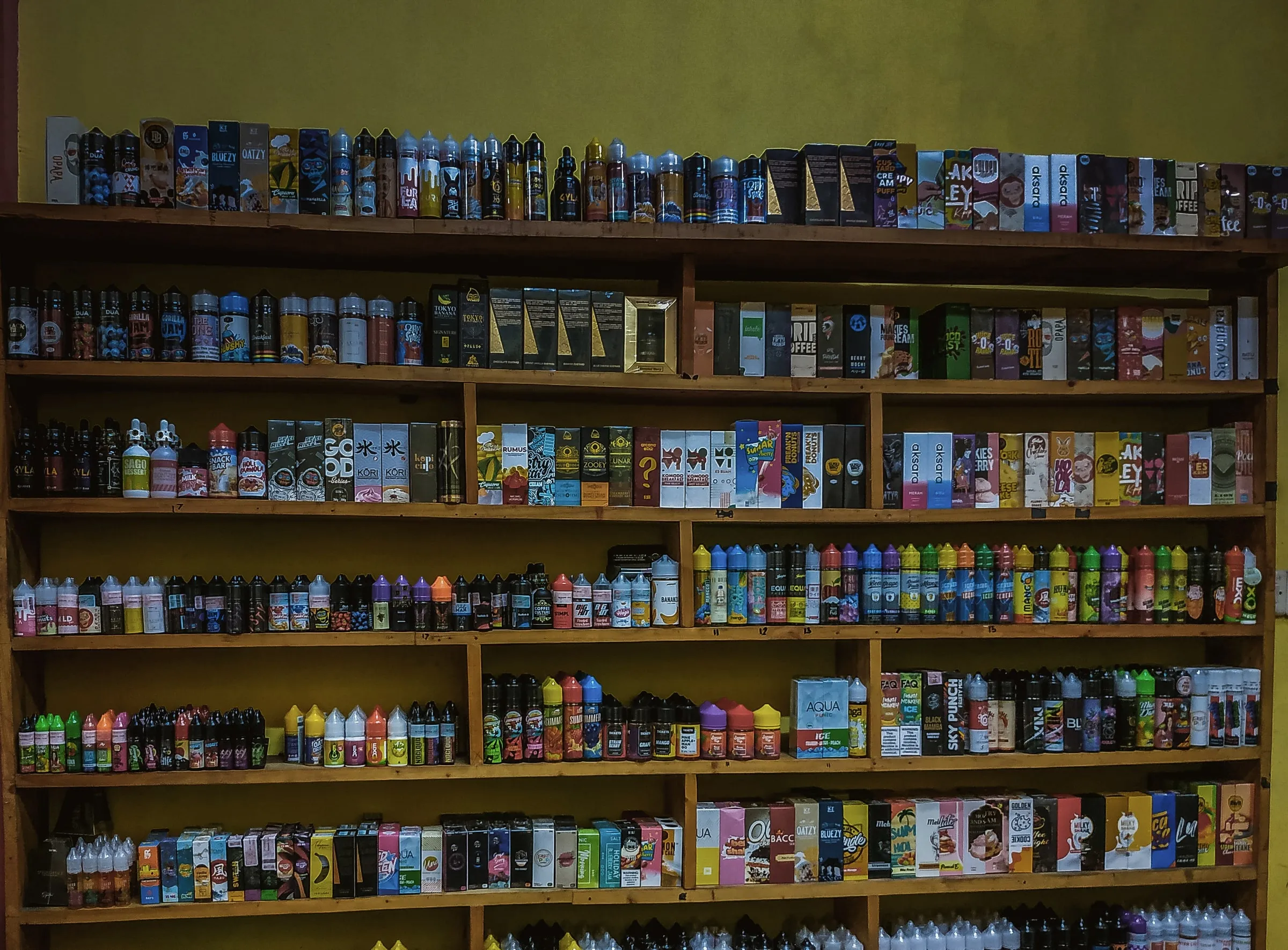 Shelves stocked floor to ceiling with vape juice bottles and boxed vaping products in a smoke shop