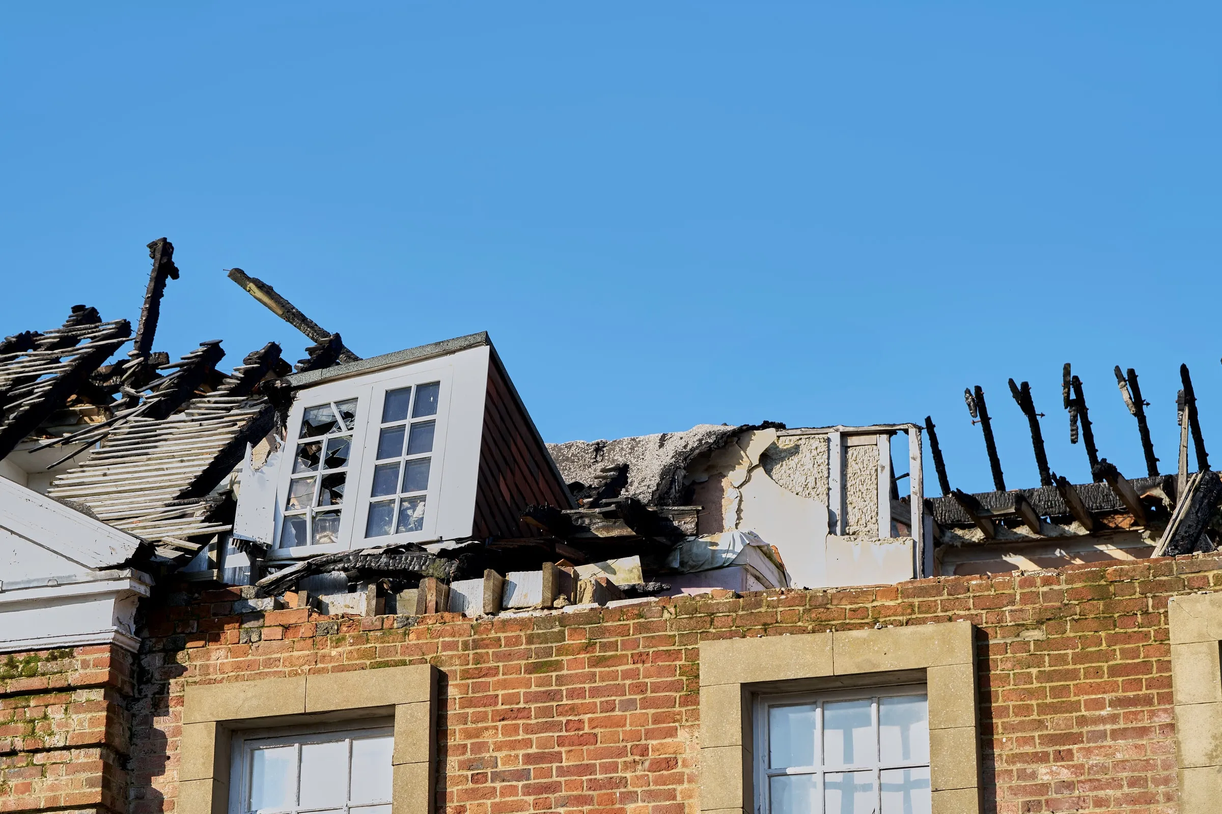 Brick building with a burned-out roof, charred rafters exposed against a blue sky