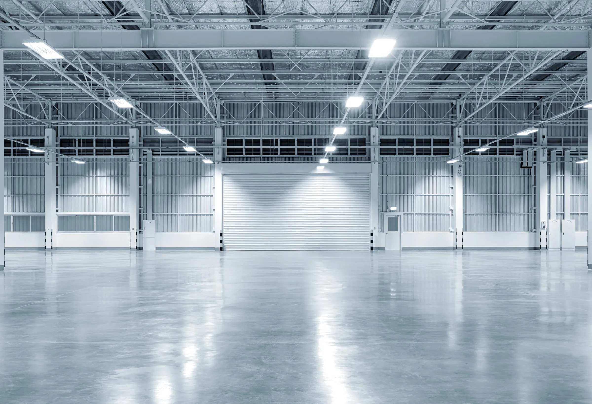 Empty warehouse interior with a polished concrete floor, skylights and white steel roof trusses
