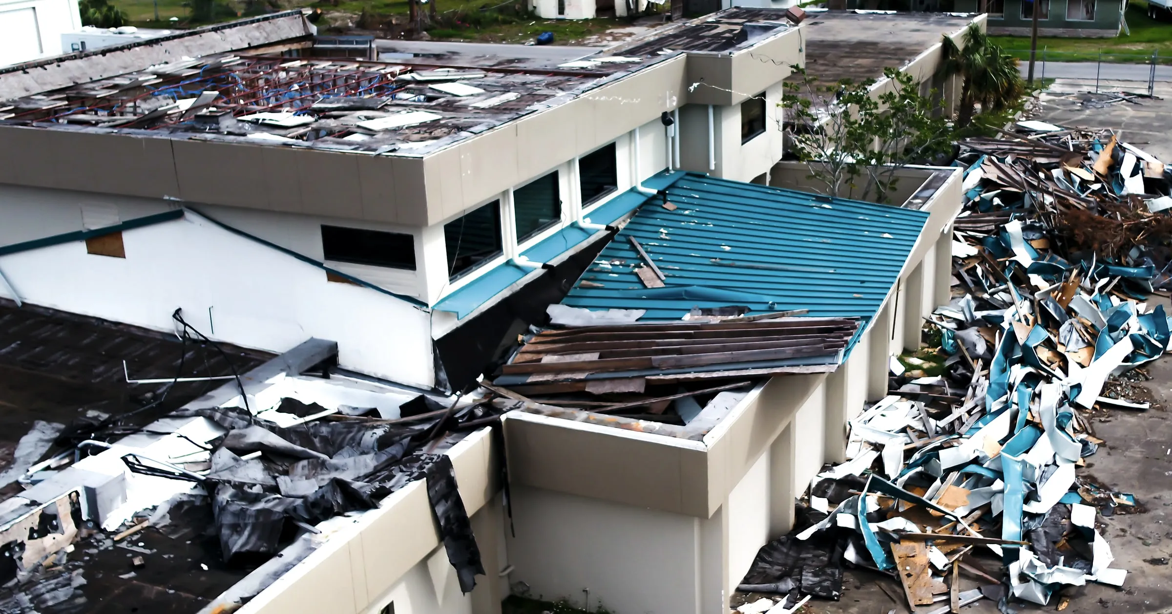 Aerial view of a building with its metal roof torn off and debris scattered around it