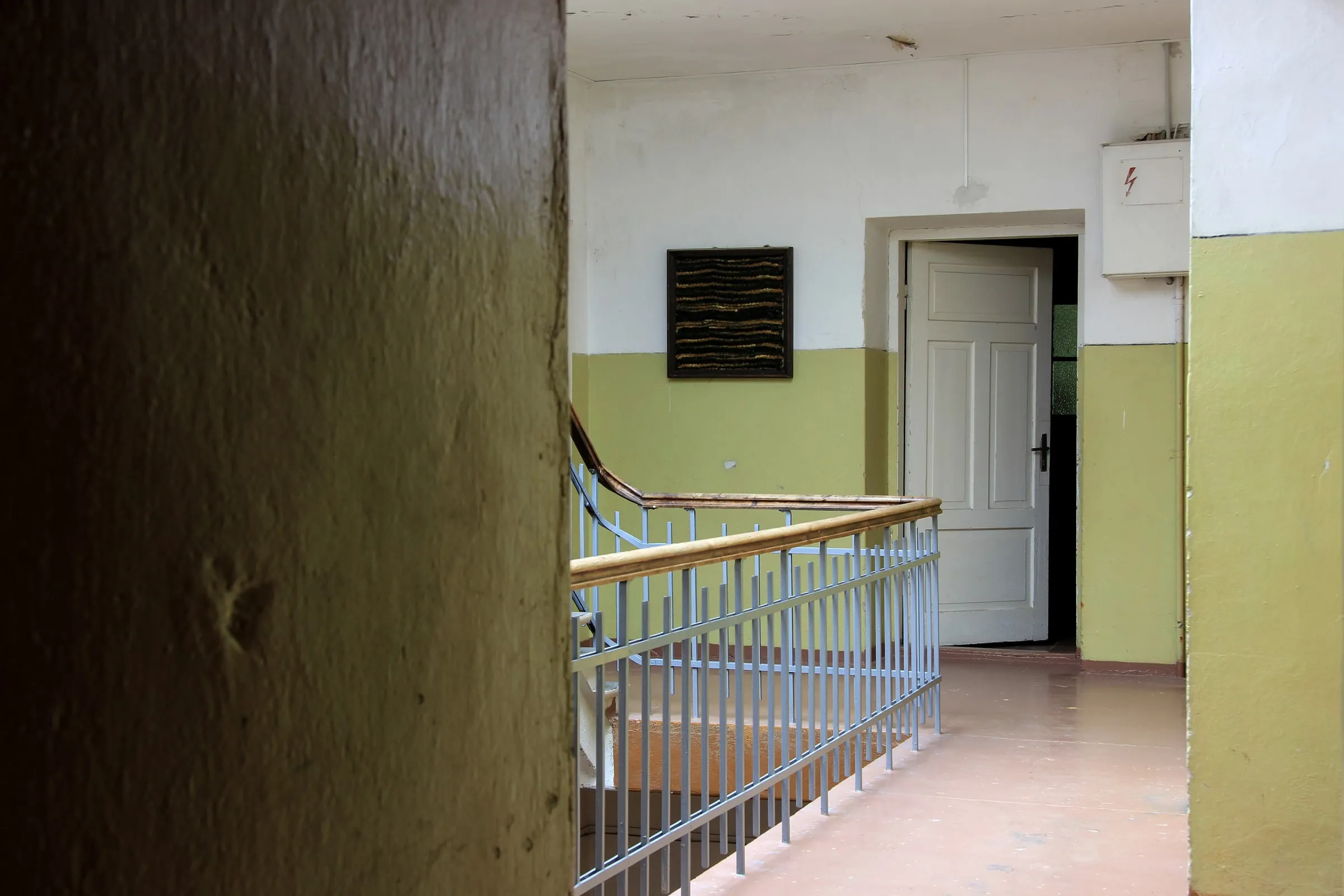 Empty apartment stairwell with worn green walls and a metal railing