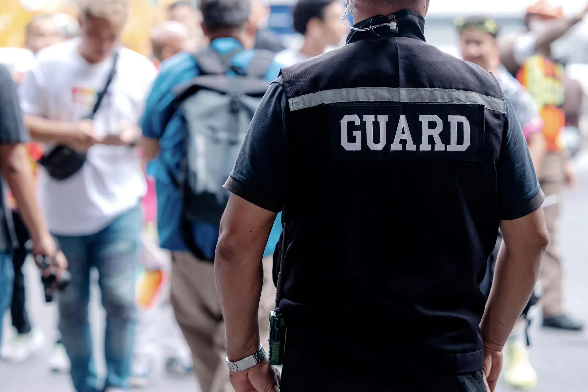 Back of a security officer in a black GUARD shirt in a crowd of people