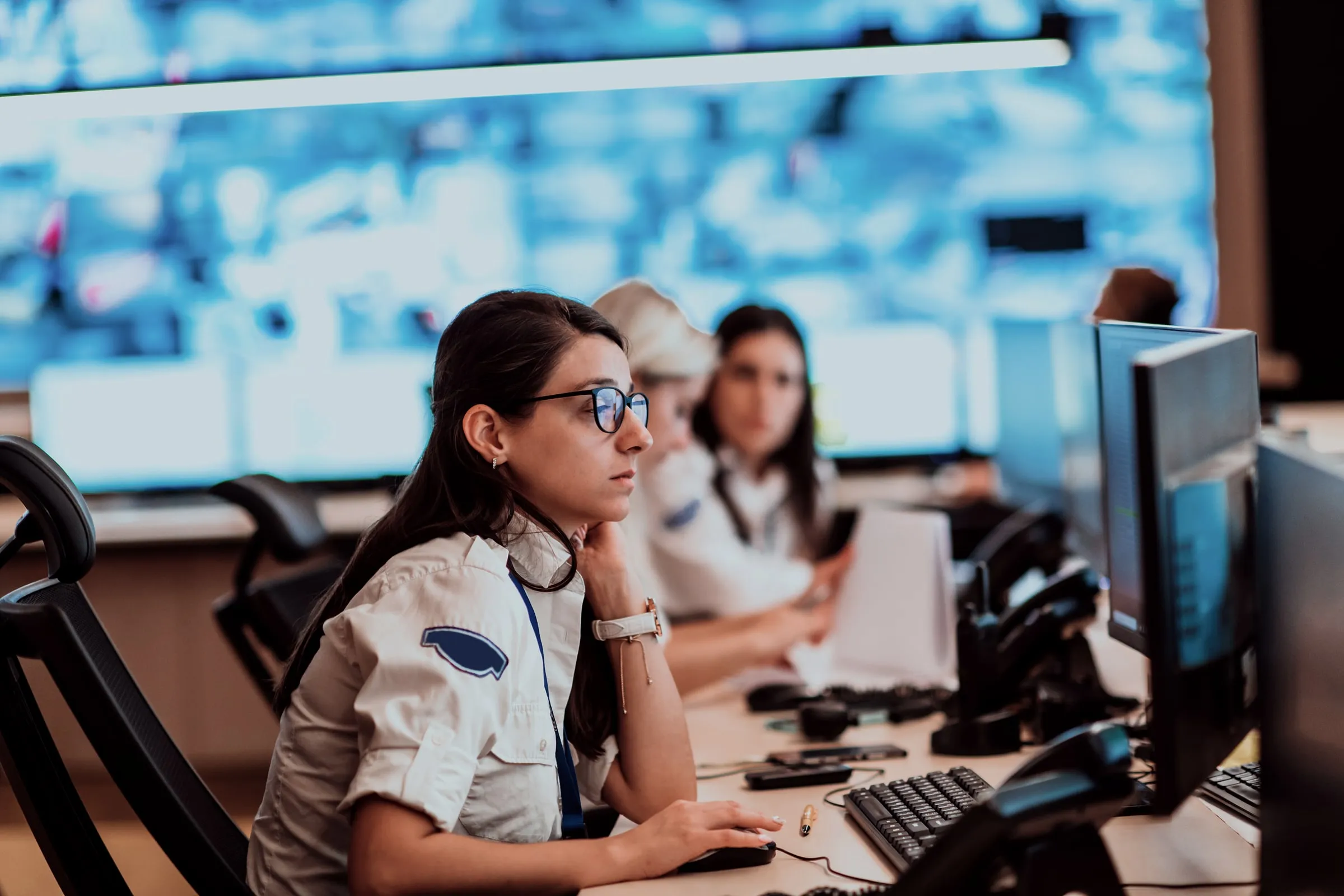 Woman with glasses at a monitor in a security operations room, colleagues behind her