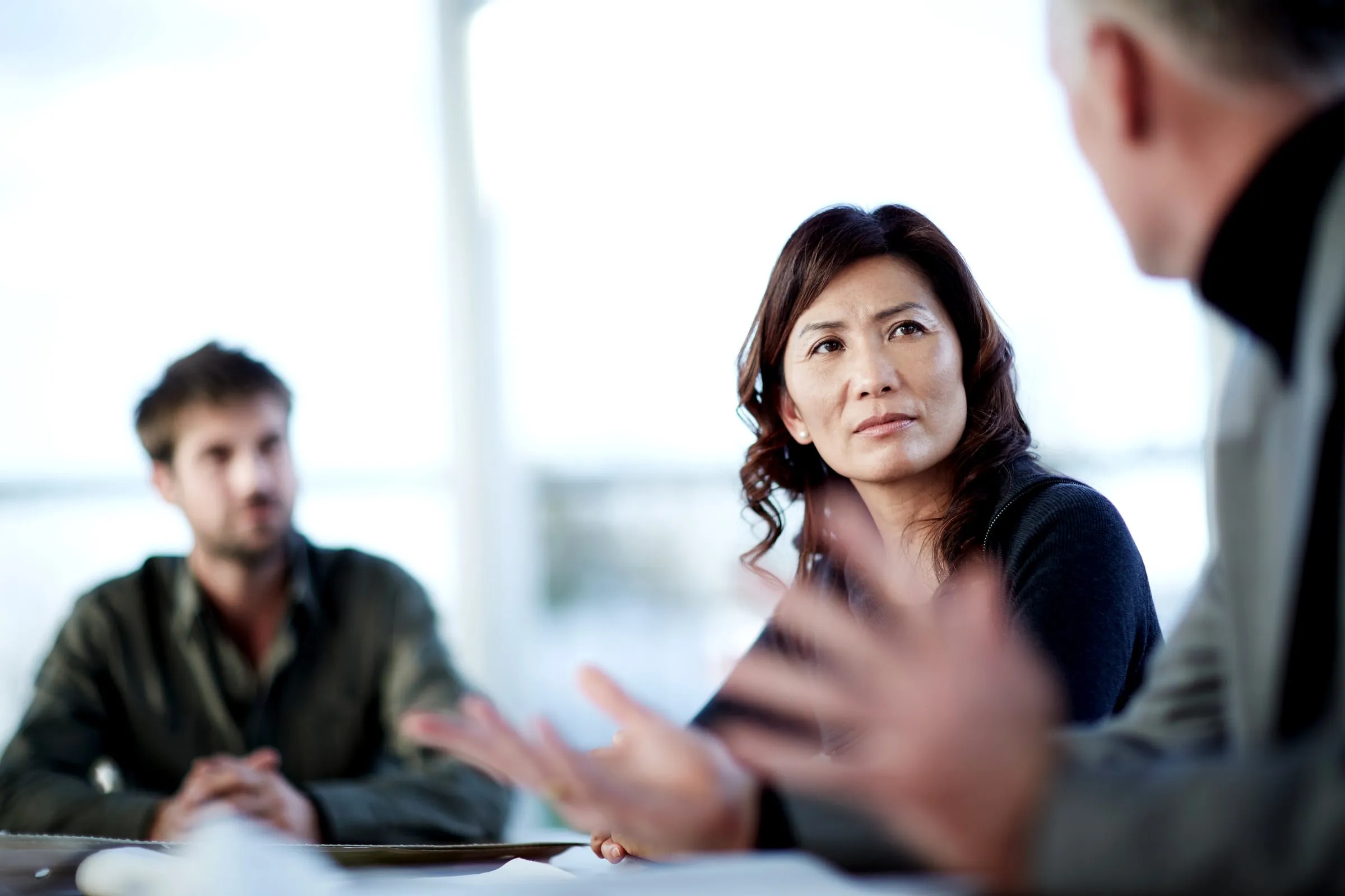 Two people at a desk in a serious conversation with a third person, seen from behind