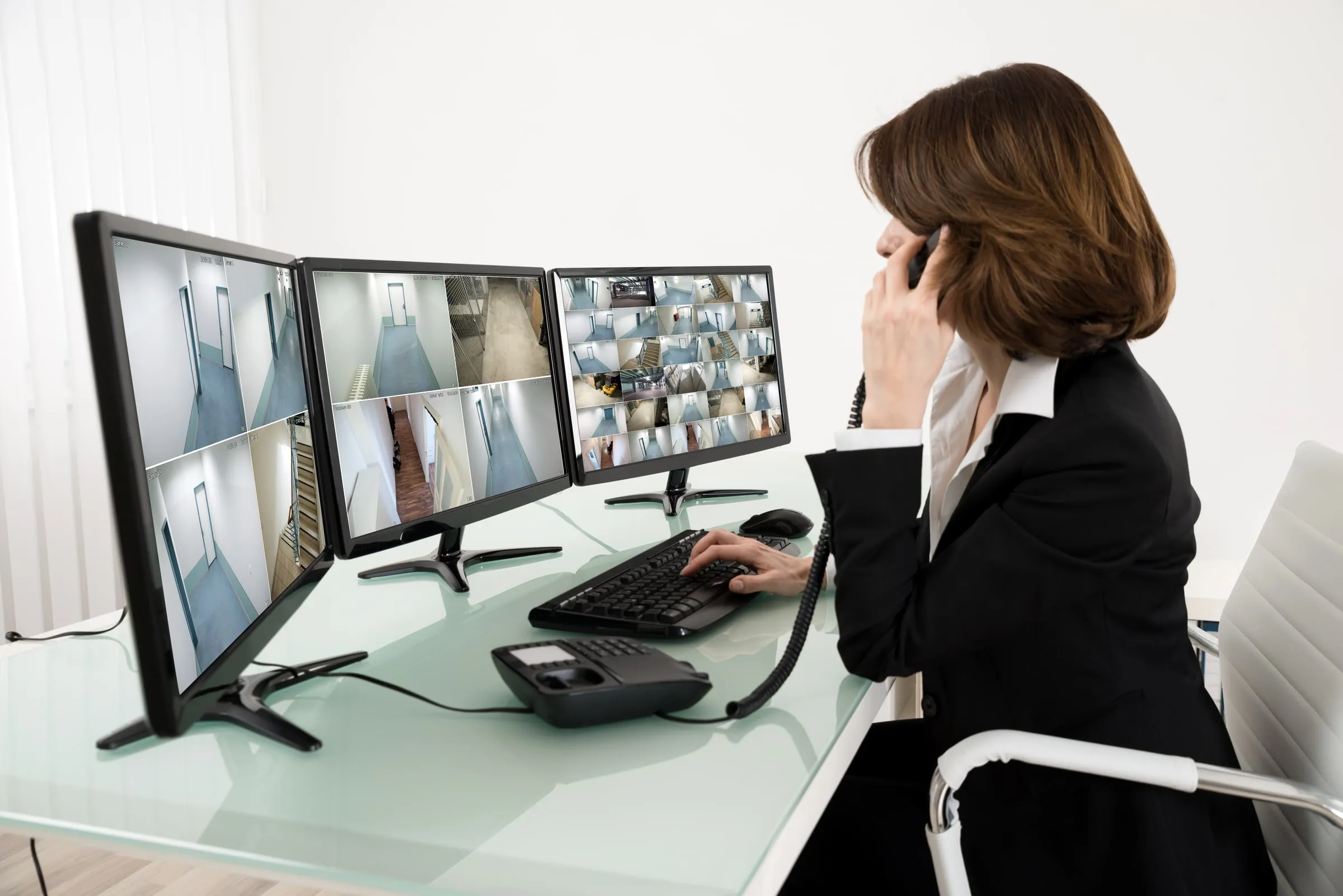 Woman at a desk looking at security camera feeds on multiple monitors
